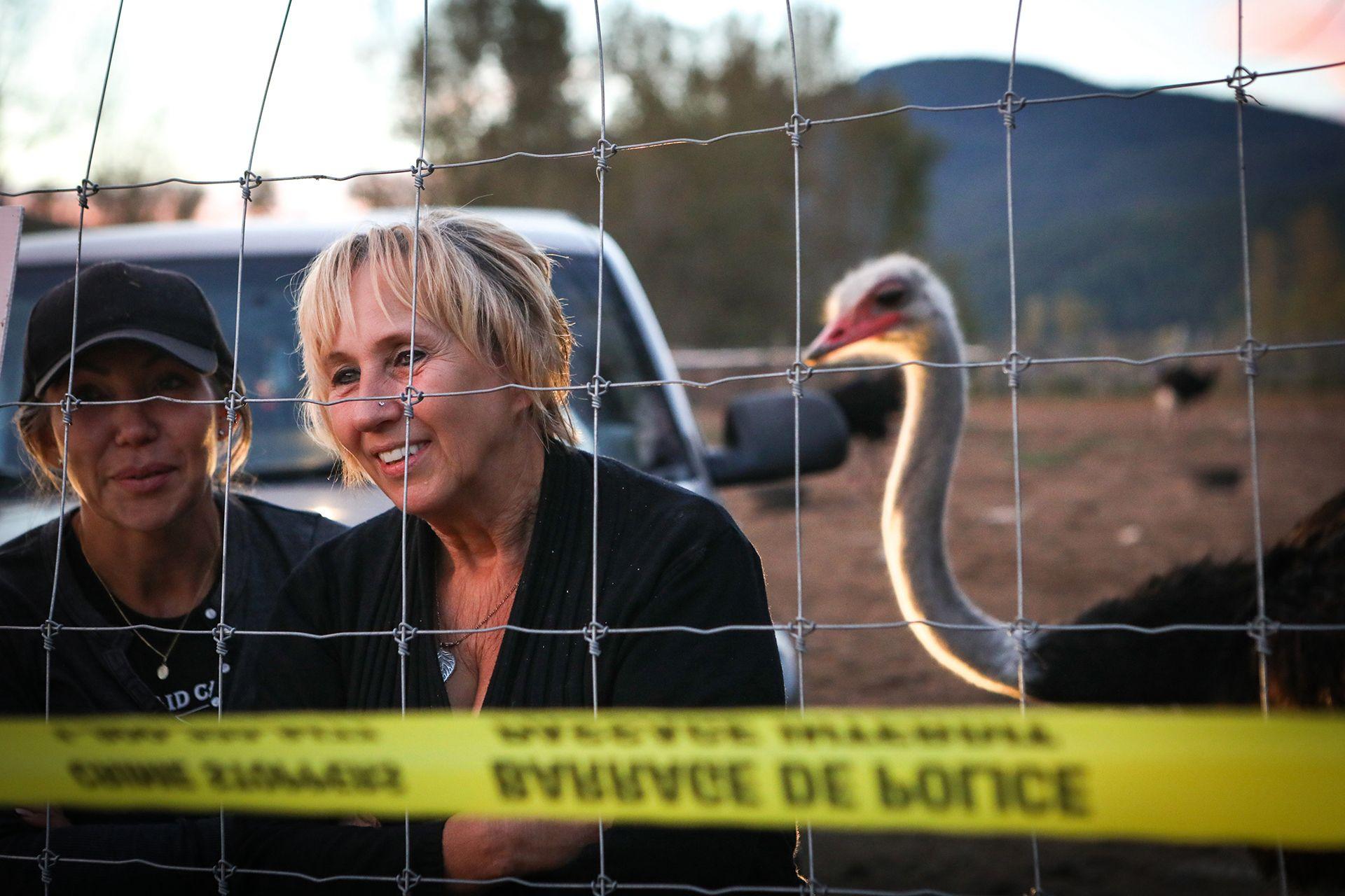 Karen Espersen, her daughter, Katie Pasitne, and an ostrich stand behind a chain-linked fence cordoned off with yellow police tape