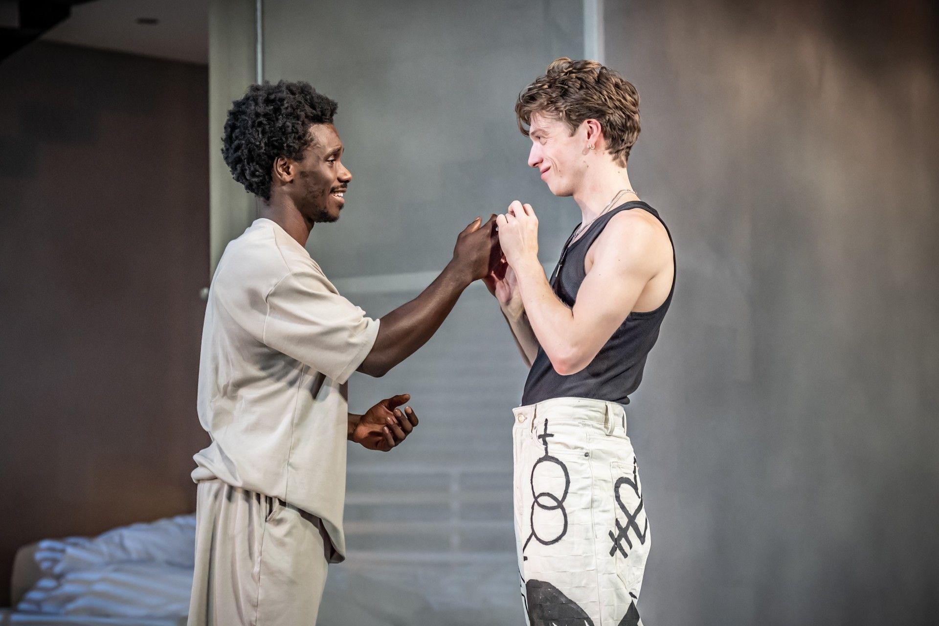 Two male actors are seen holding hands on stage.