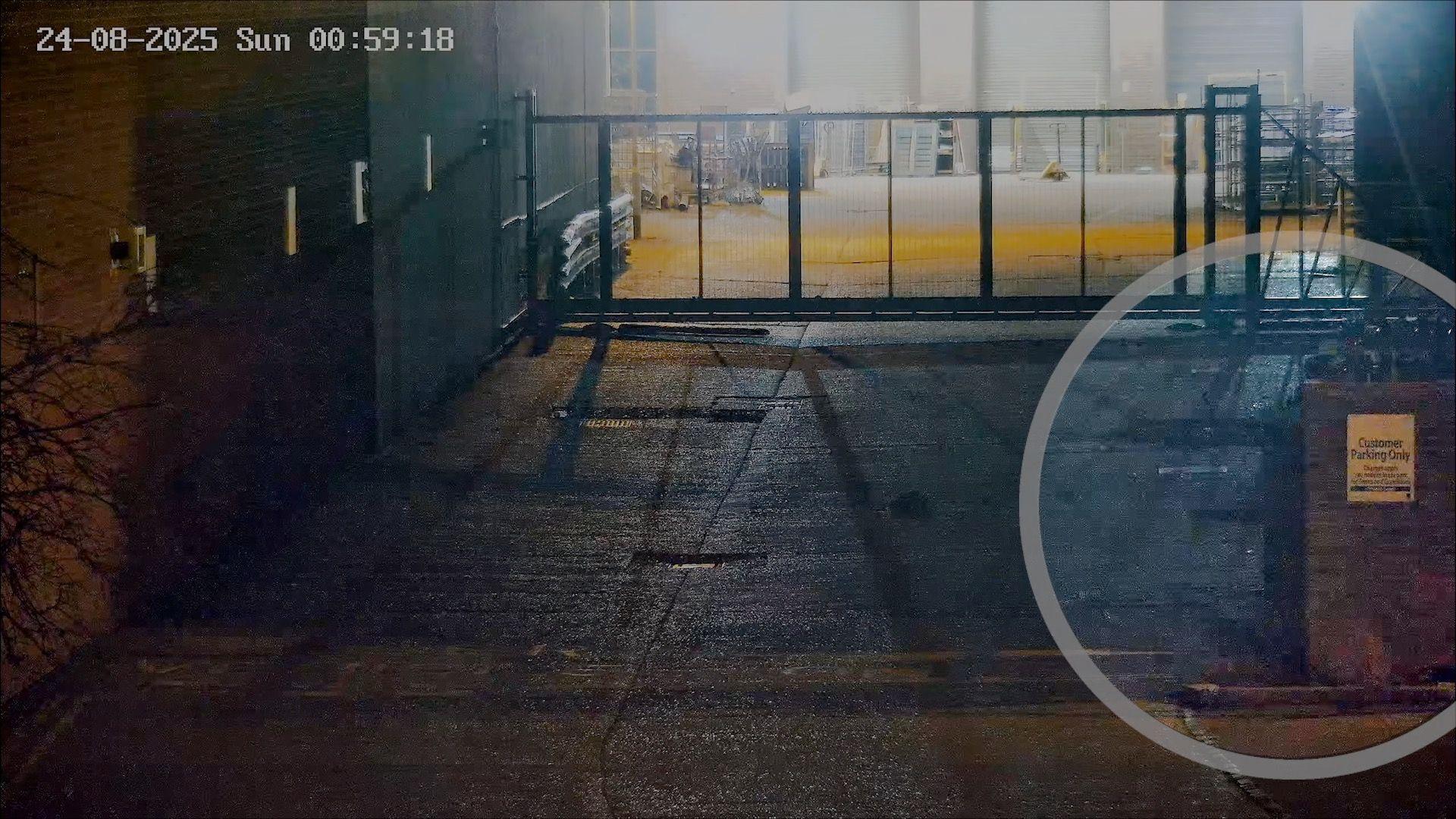 Night-time CCTV of a locked security gate across an industrial yard, timestamped 00:59 on 24 August 2025.