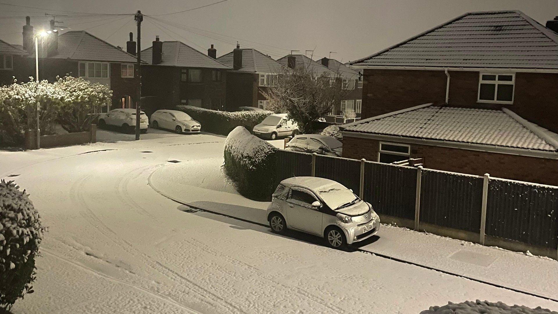 Urban night-time scene showing rooftops, cars and roads covered in snow.