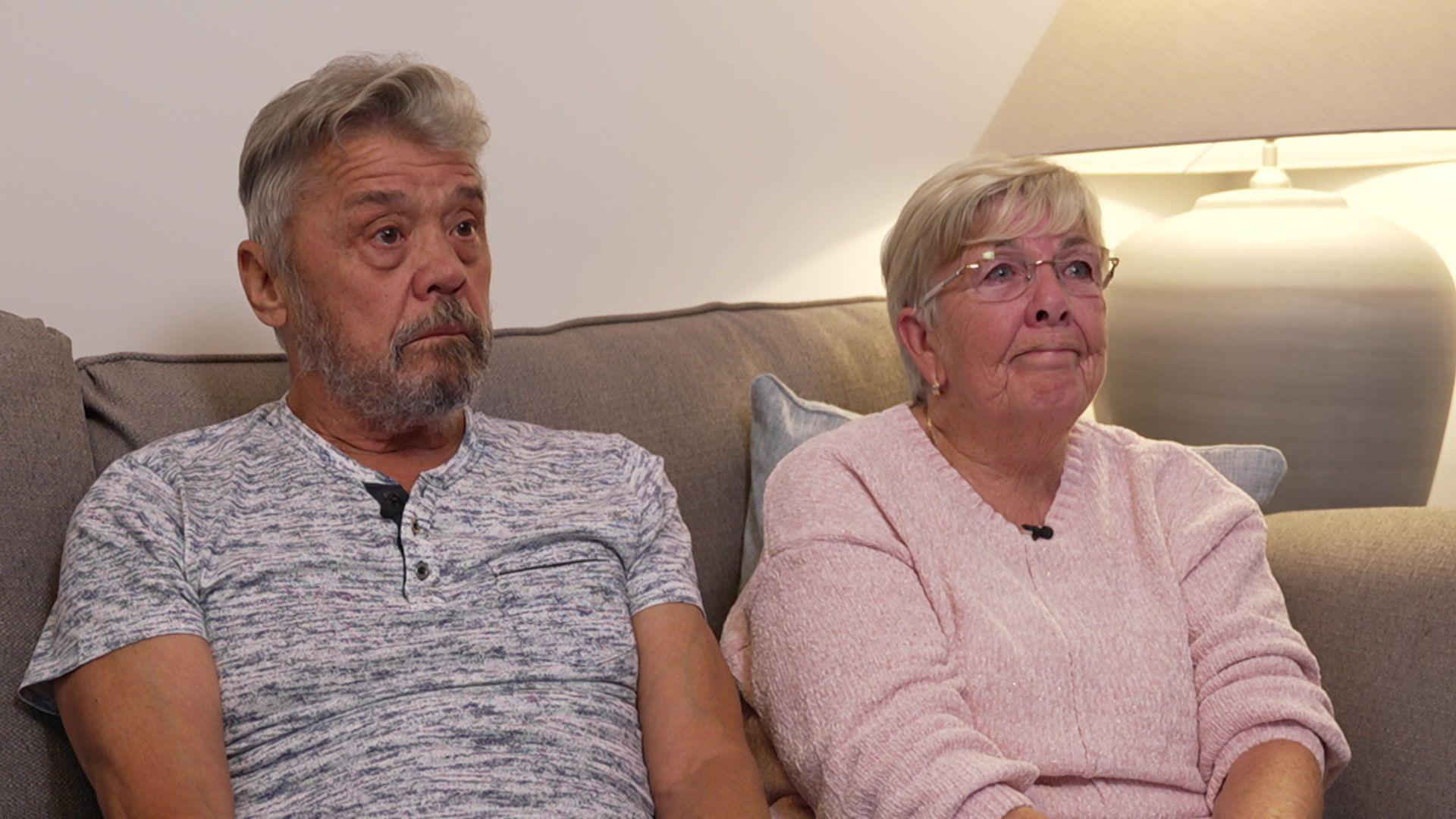 An older Eddie and Lin sit on a sofa in their living room. Lin is nearly in tears