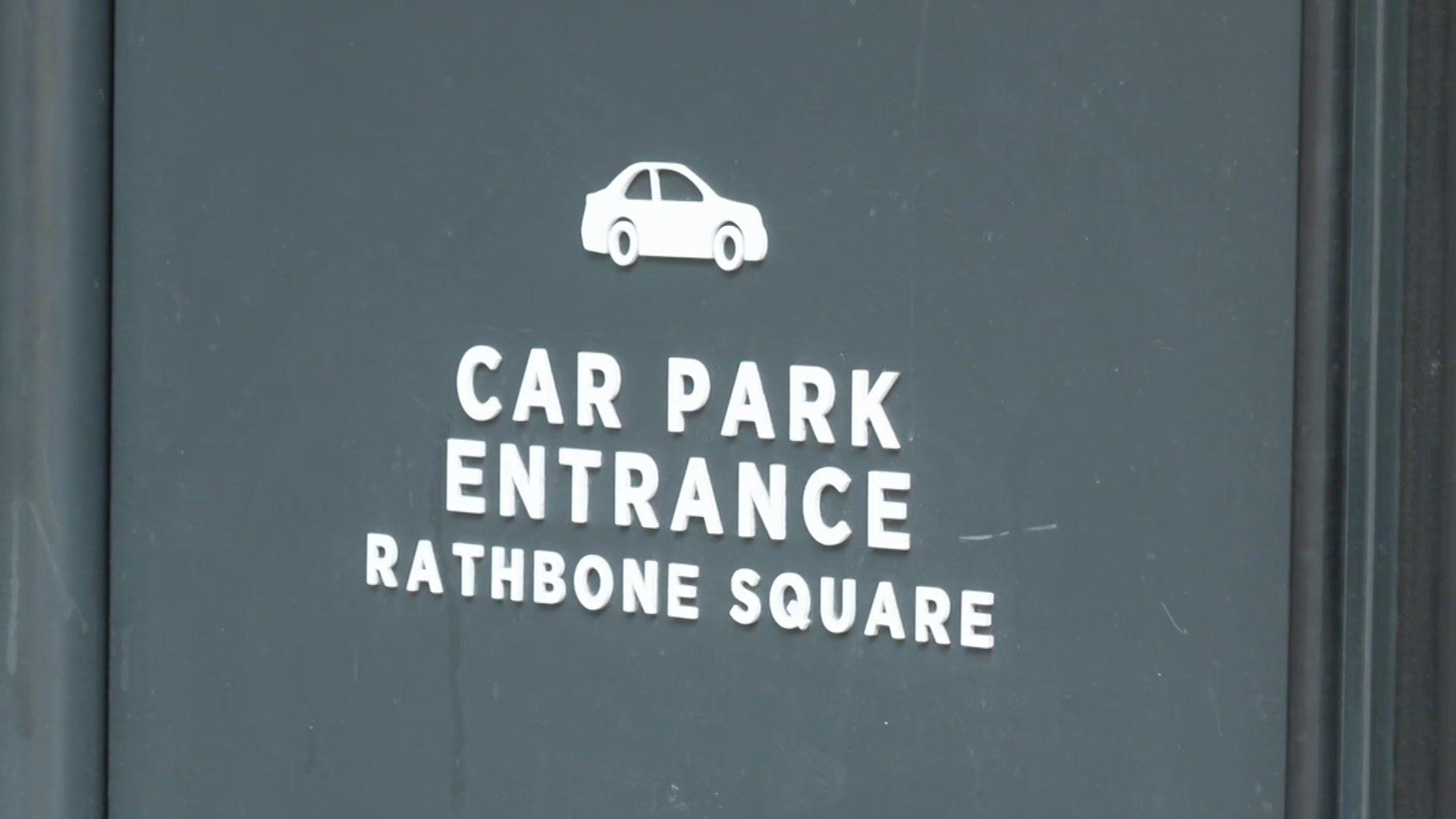 Sign reading "Car Park Entrance Rathbone Square" with a simple white icon of a car above the text on a dark background.