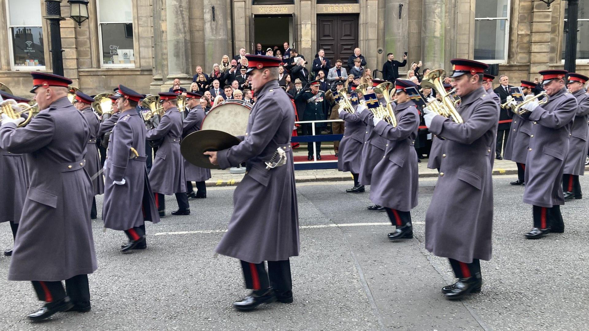 An Army band marches through Sunderland. Soldiers in uniform are playing trumpets and drums while marching past a crowd watching the procession.