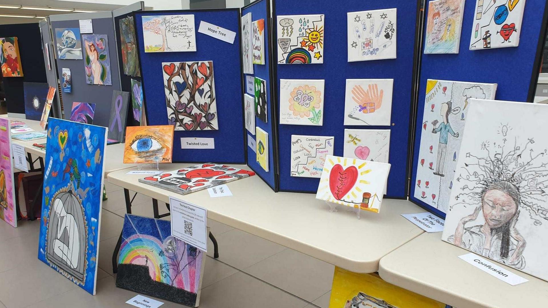 Trestle tables with noticeboards on them - different artworks on all sizes of canvas are pinned to the boards and lean against the tables.