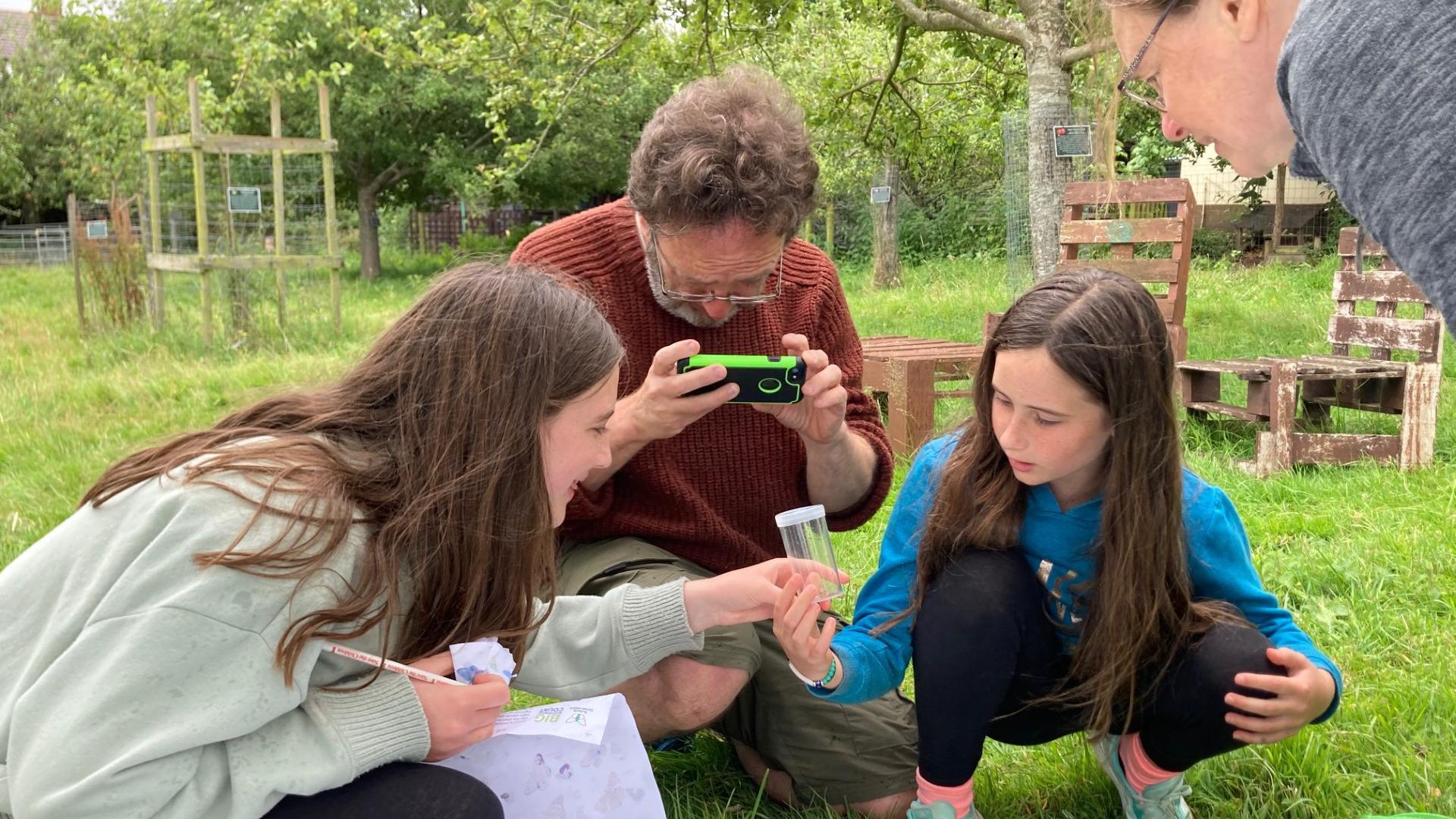 Two girls and a man observing wildlife in a field