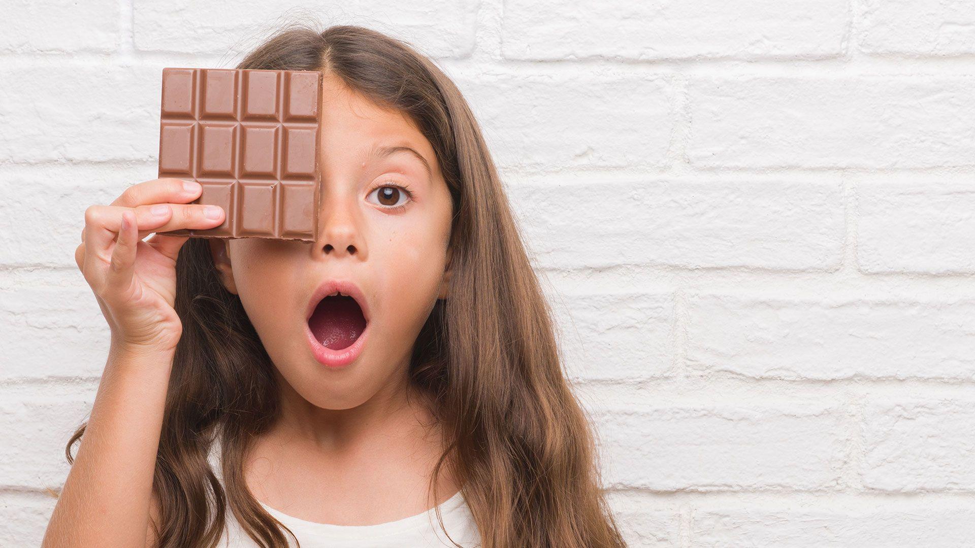 A child holding a bar of chocolate over their face with a surprised expression