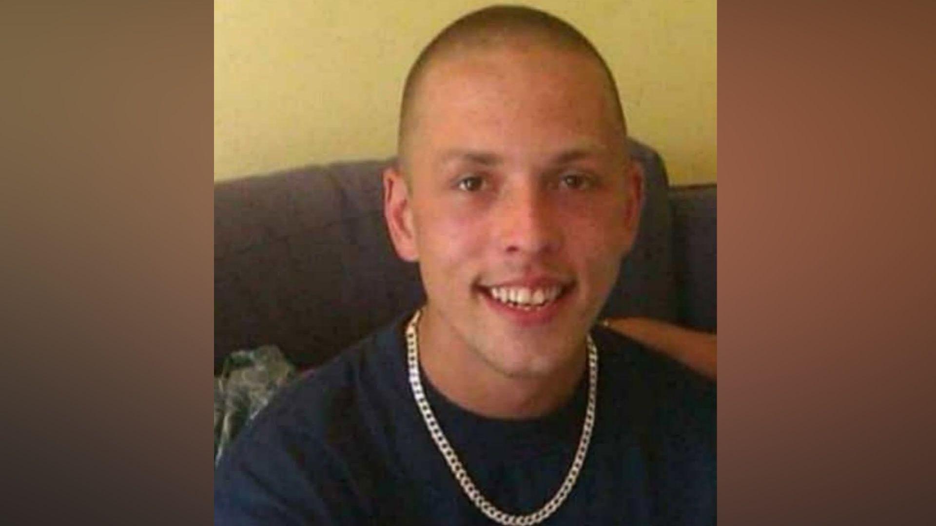 Photograph of Gareth Chumber-Kelly sitting indoors wearing a dark T-shirt and chain necklace.