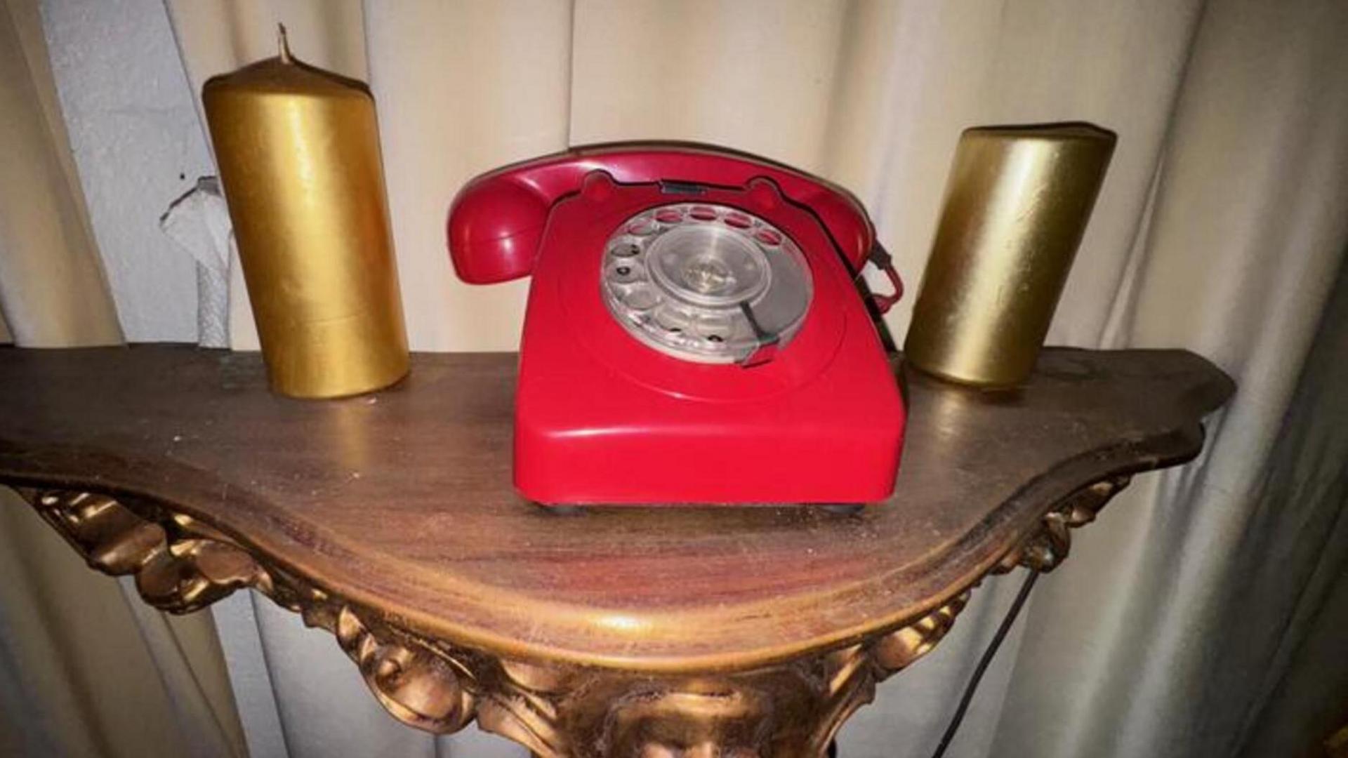 A red communications hotline phone and two gold candles