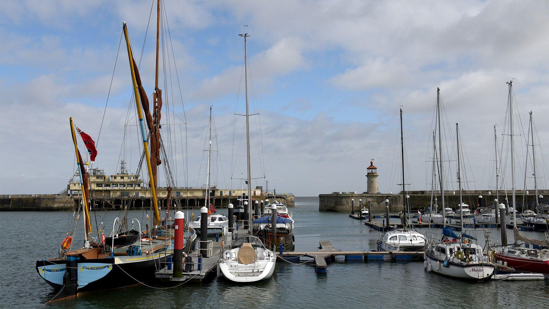 A harbour with many boats with tall sails moored closely together.