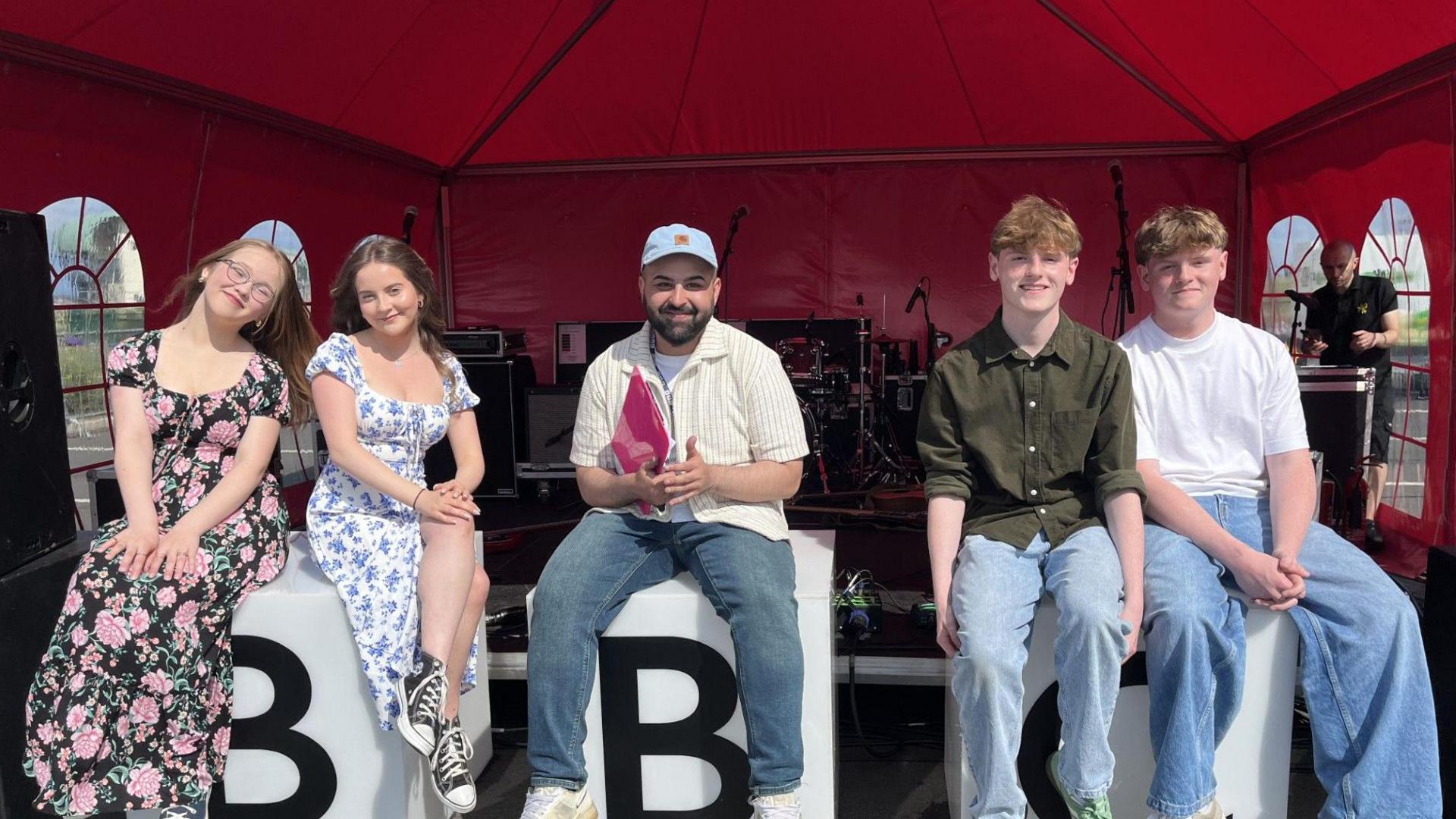 The Last Time band members - two female and two male - sit on blocks with the letters of BBC on them. Two band members sit on the left and right of Shakk, the presenter of BBC Introducing North East.