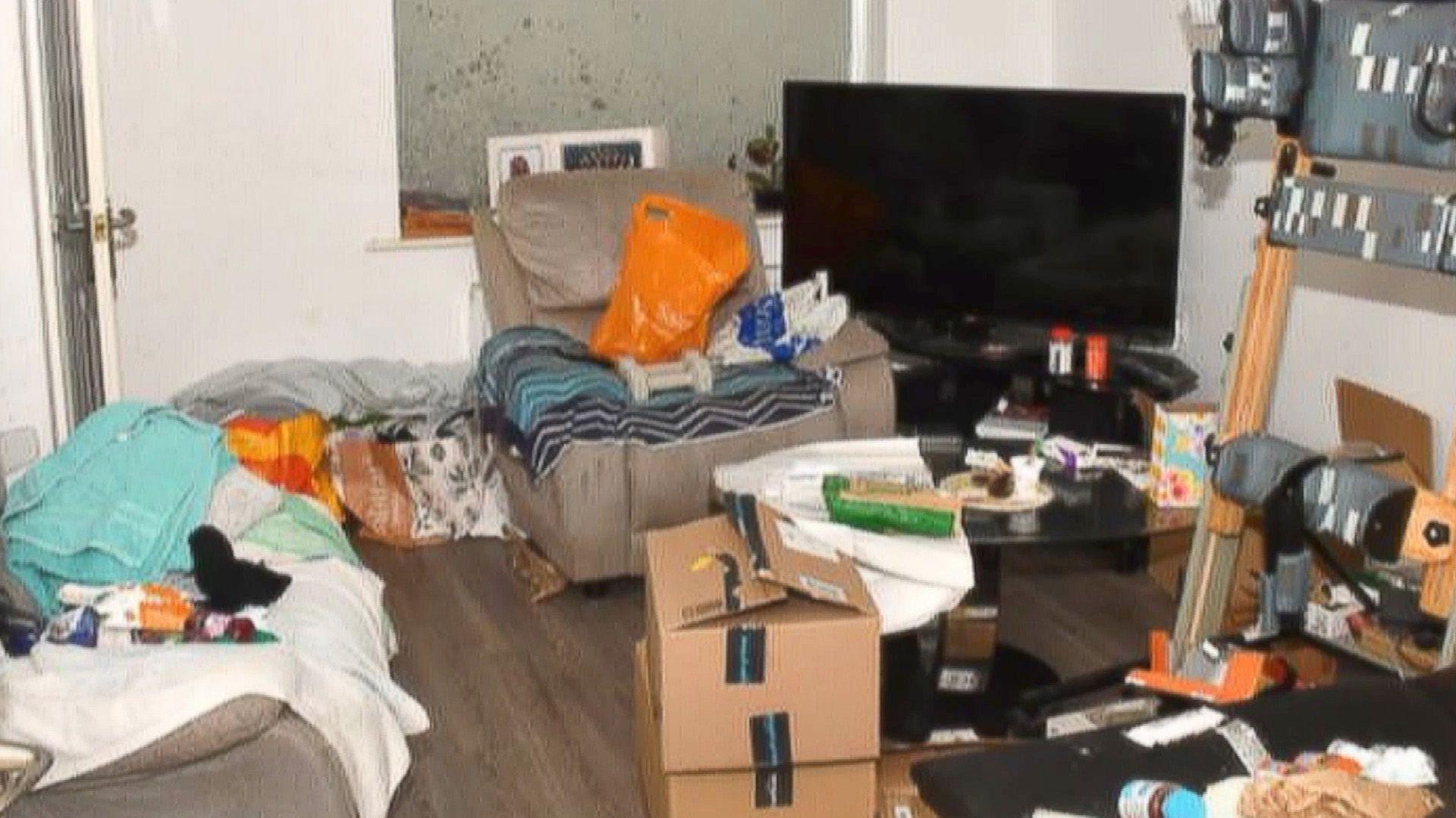 Police picture of Rudakubana's living room. There is laminate flooring and a drawn blind, and black TV, with boxes, plastic bags and other items strewn around the room.