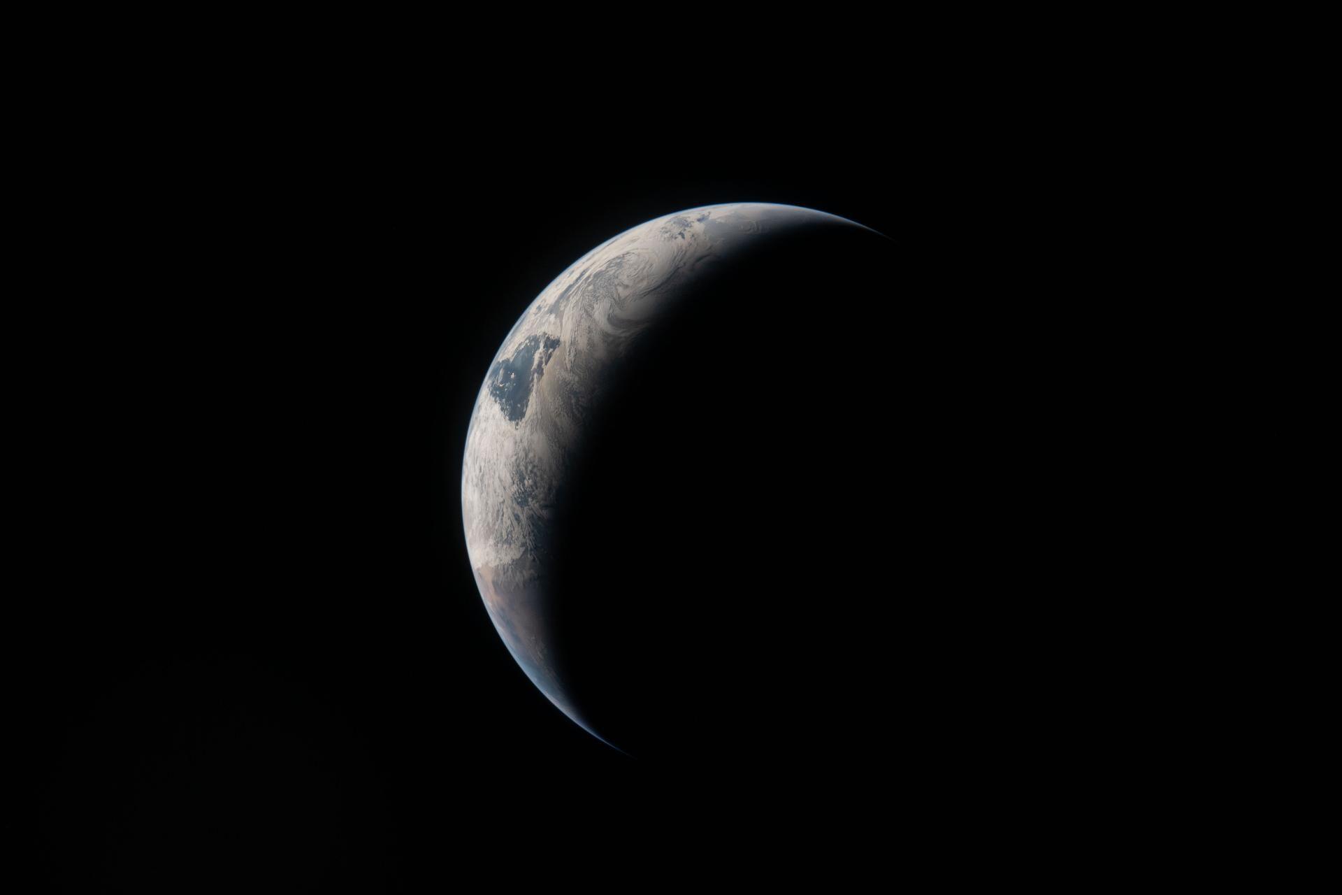 A cresent view of the Earth with sunlight falling on th eright side of its surface in the blackness of space.