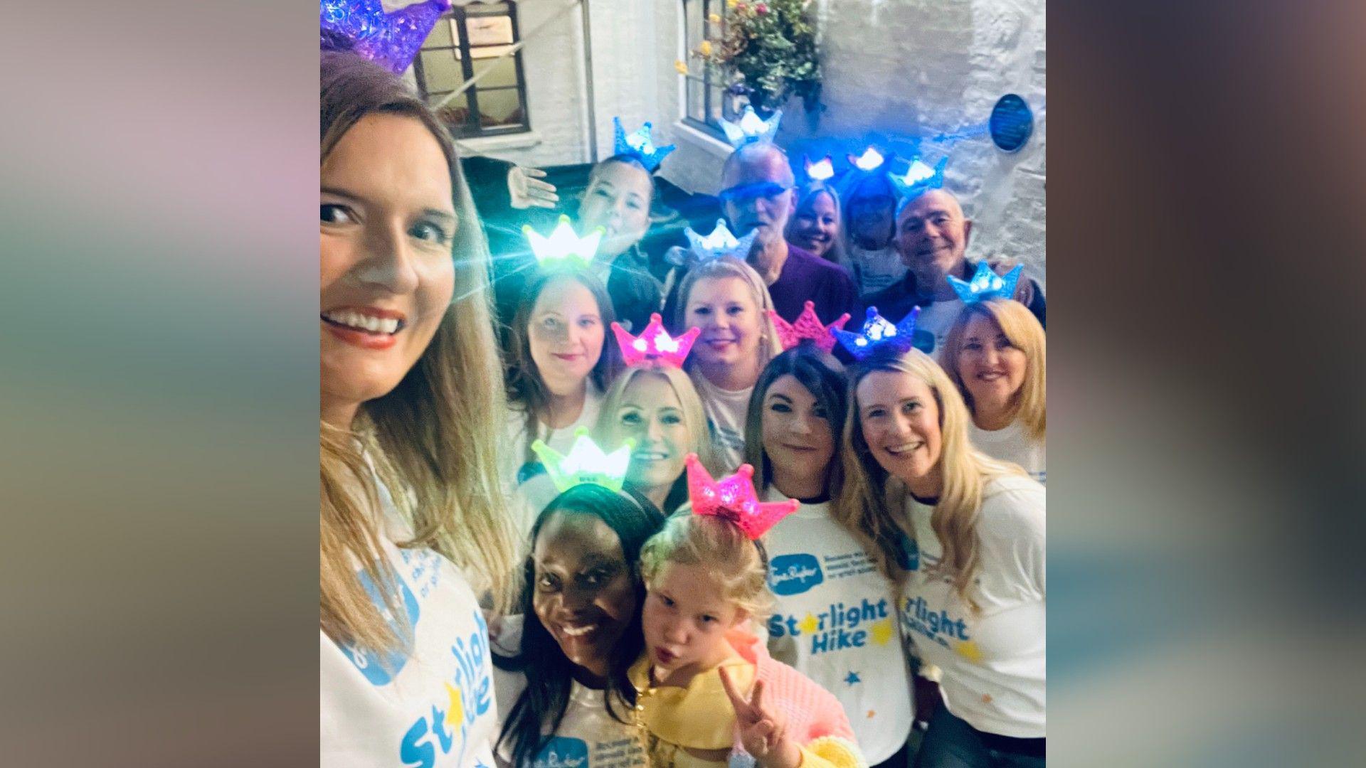 Group of women and men - wearing white T-shirts and colourful lit crowns on their heads - posing for a selfie