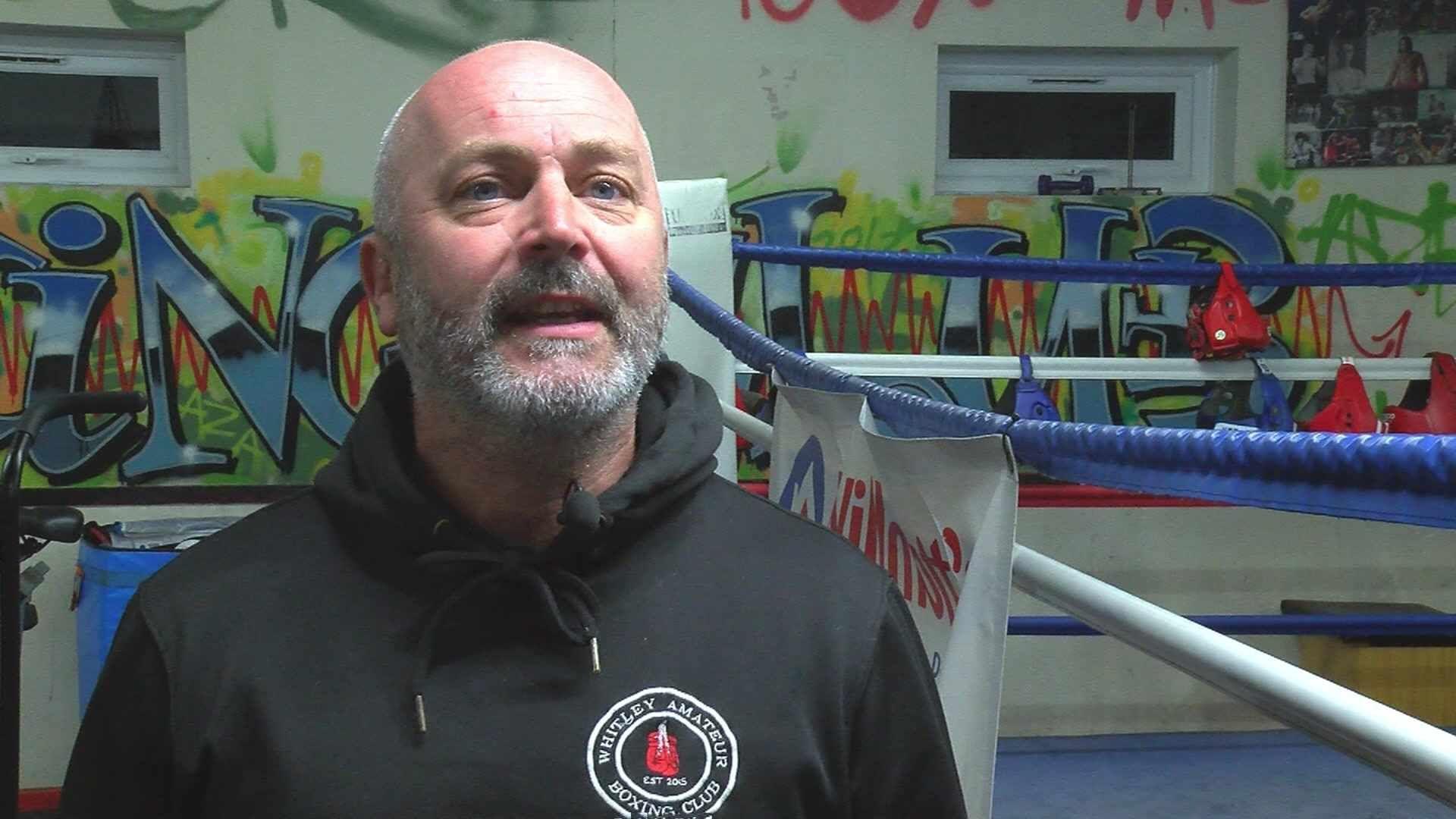 Danny looking straight to the camera, had blue eyes and grey facial hair. He is wearing a black hoodie with a logo that says Whiteley Amateur Boxing Club.