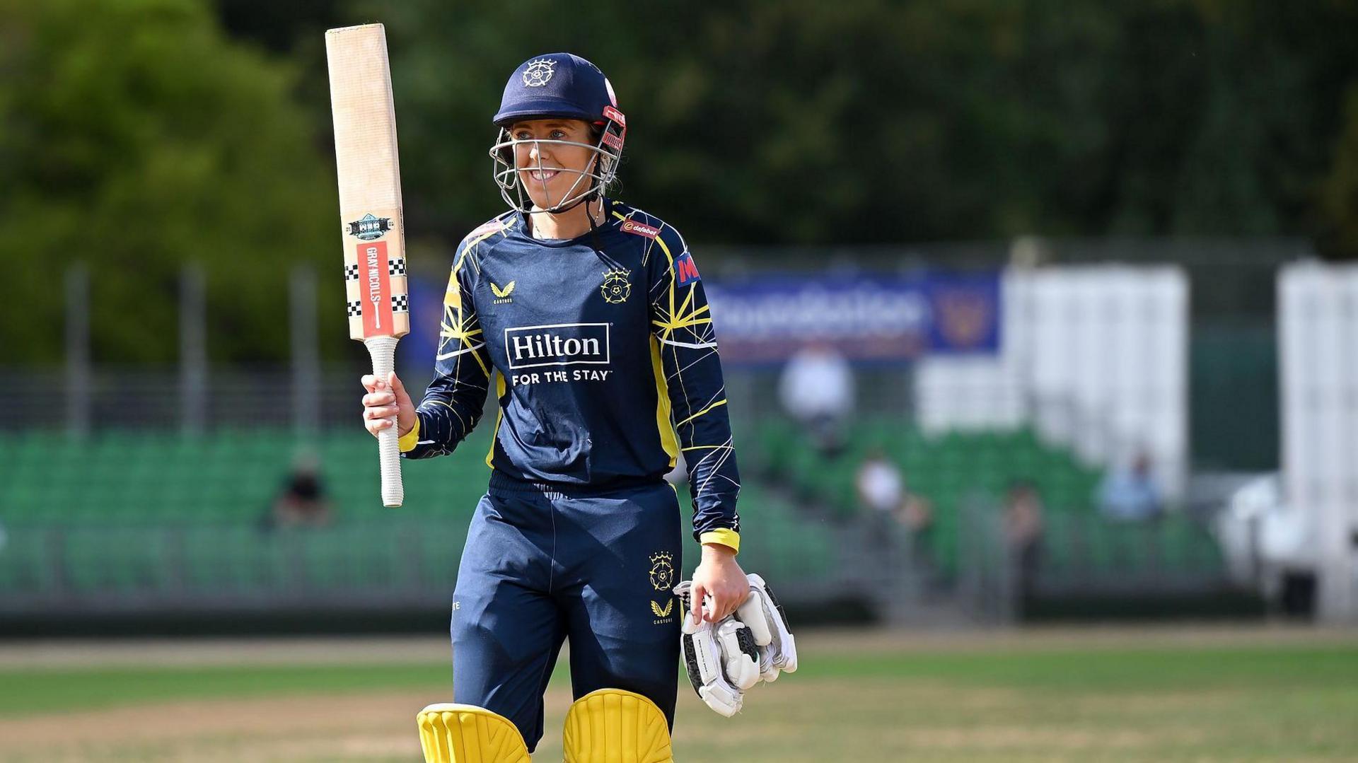 Georgia Adams raises her bat as she walks off the field after scoring a century