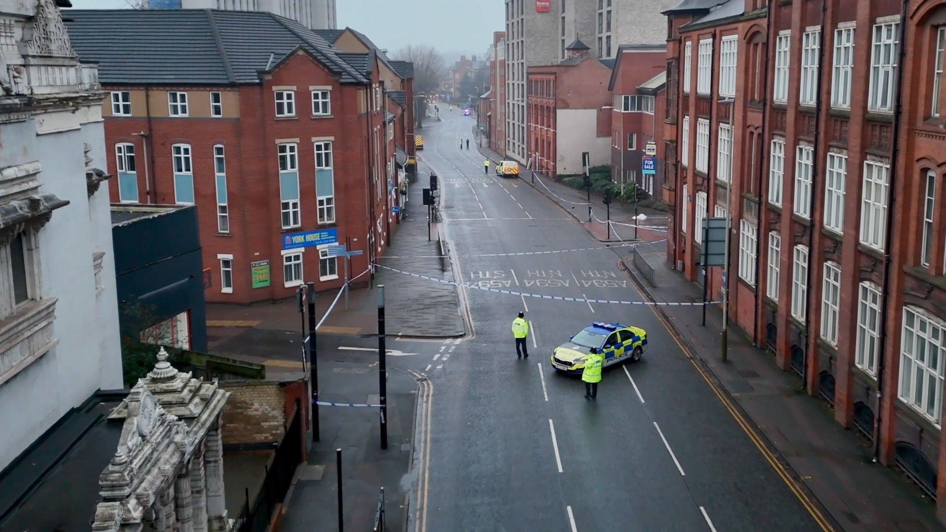 Drone shot of empty street with police car, two officers and police cordon.