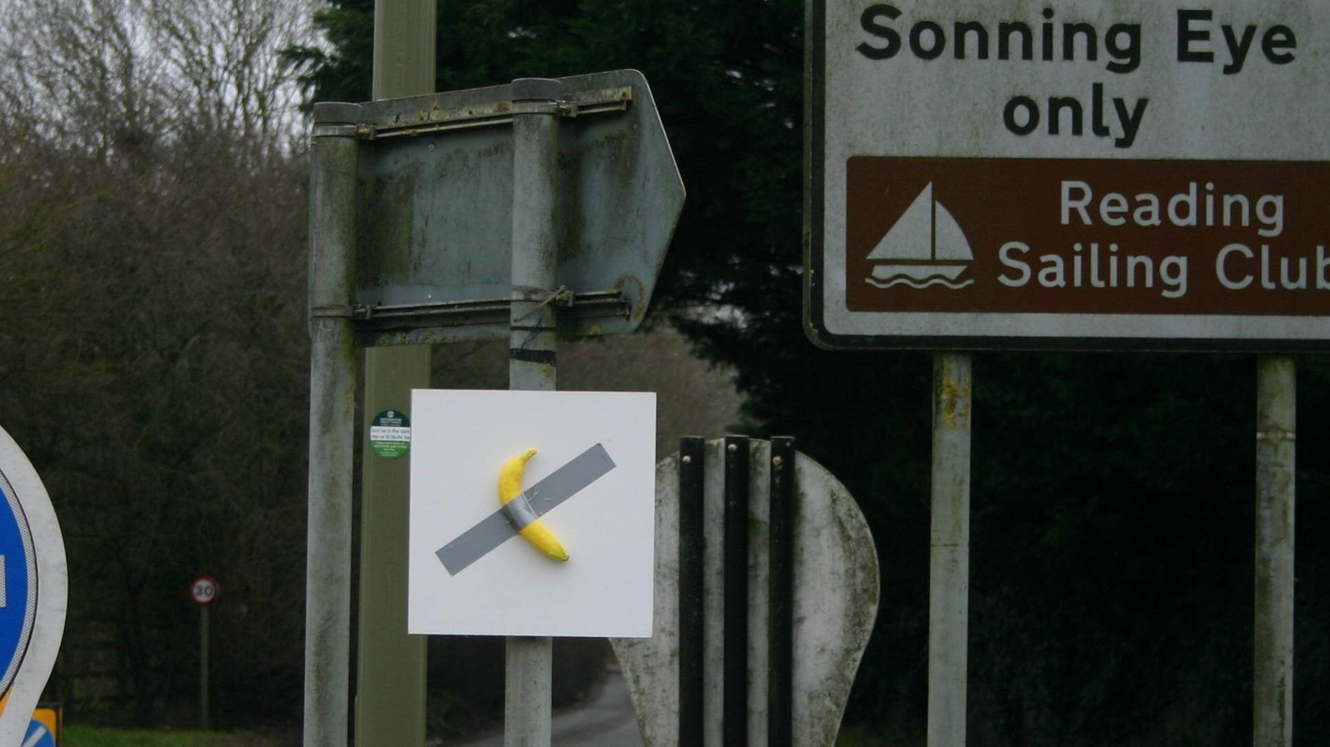 A banana duct-taped onto a white board is affixed to the pole of a street sign on a mini roundabout