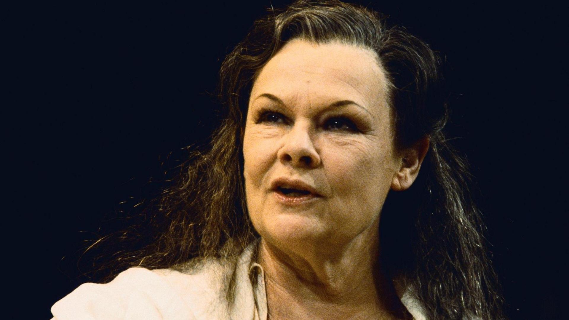 A close up of Dame Judi Dench on stage, wearing a white shirt and with long brown hair.