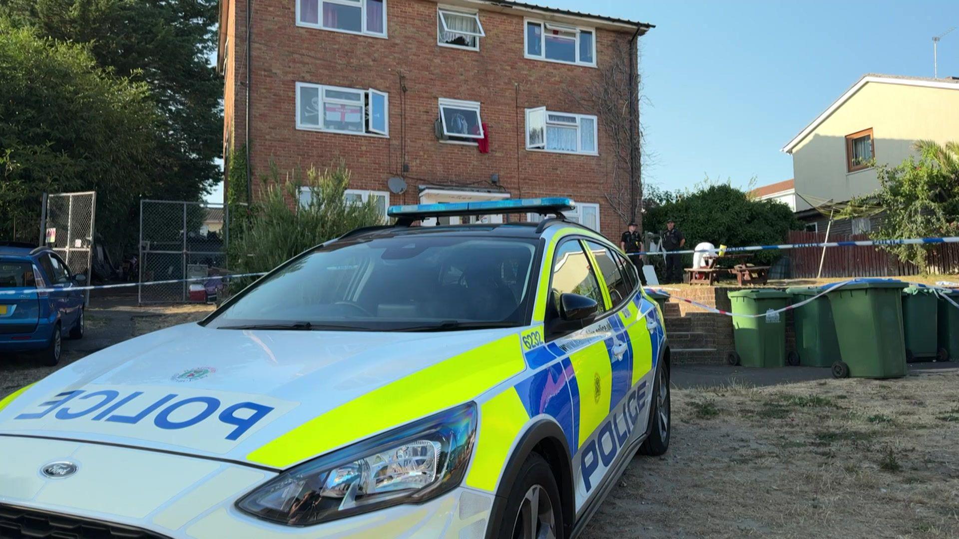 A police car is parked in front of a three-storey brick building on Weston Lane, in Southampton.