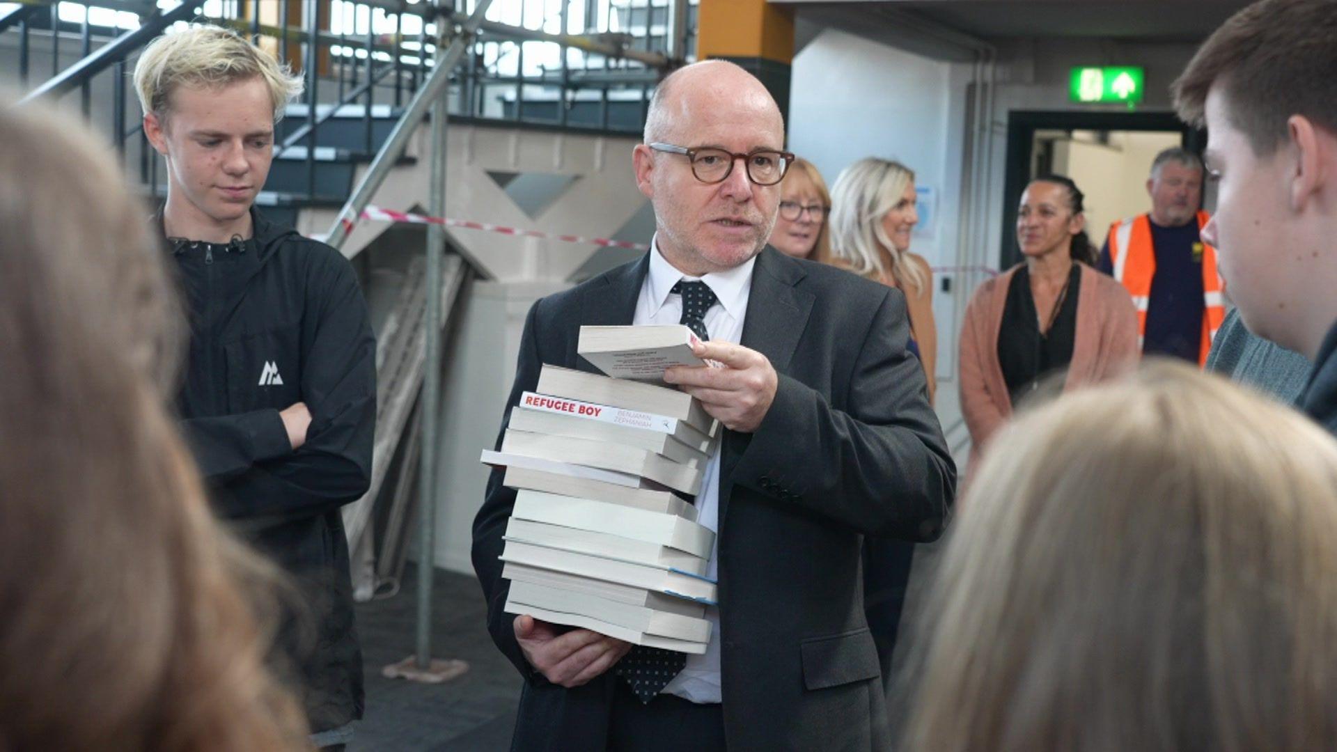 Attorney General Richard Hermer holding a stack of books in Spellow Library