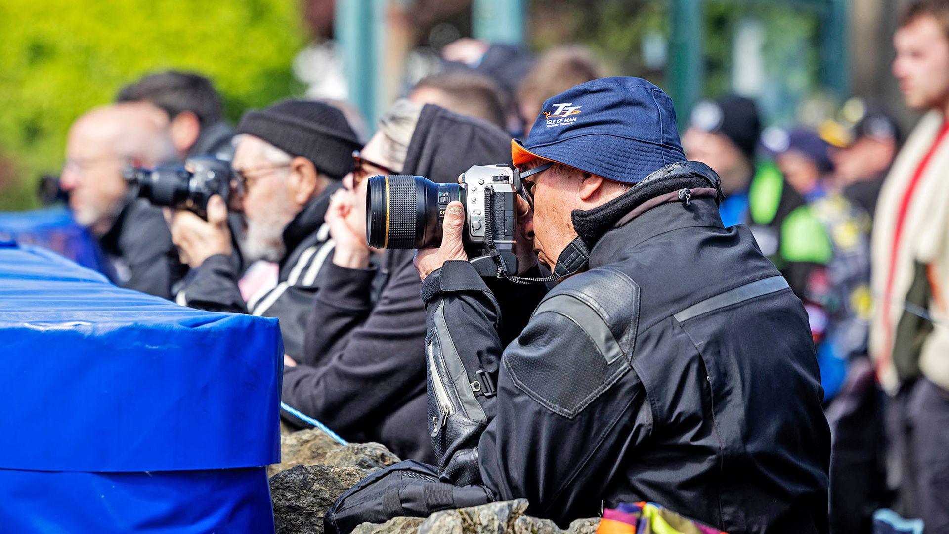 People with cameras pointed ahead sitting behind a barrier