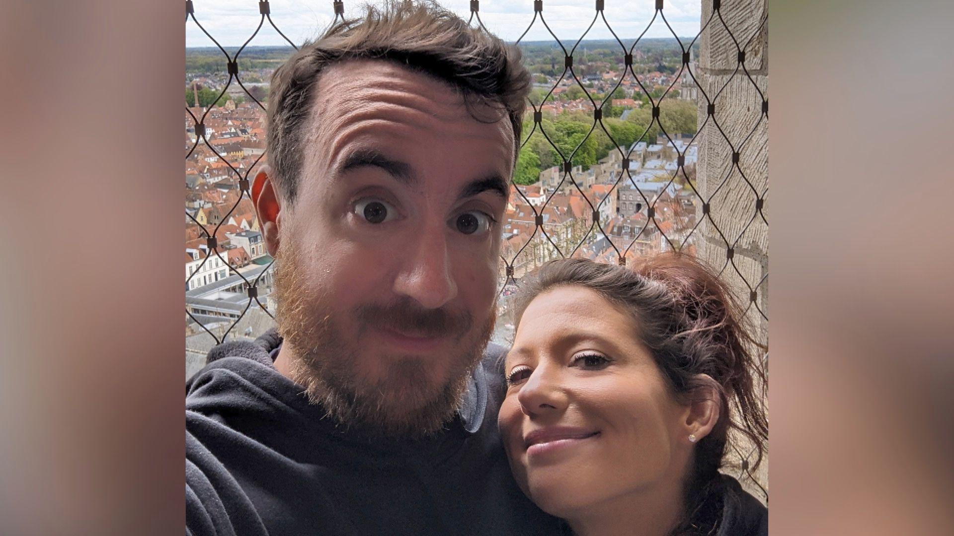 Andrew and Jennifer pose for a selfie. Andrew is wearing a dark grey hoodie, as is Jennifer. They are standing close together looking at the camera and smiling.