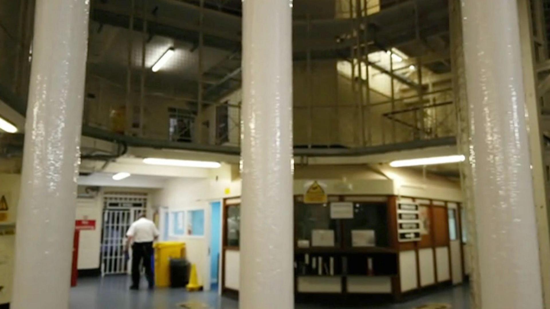 Photograph taken through three white metal bars, showing a prison officer leaving the central tower