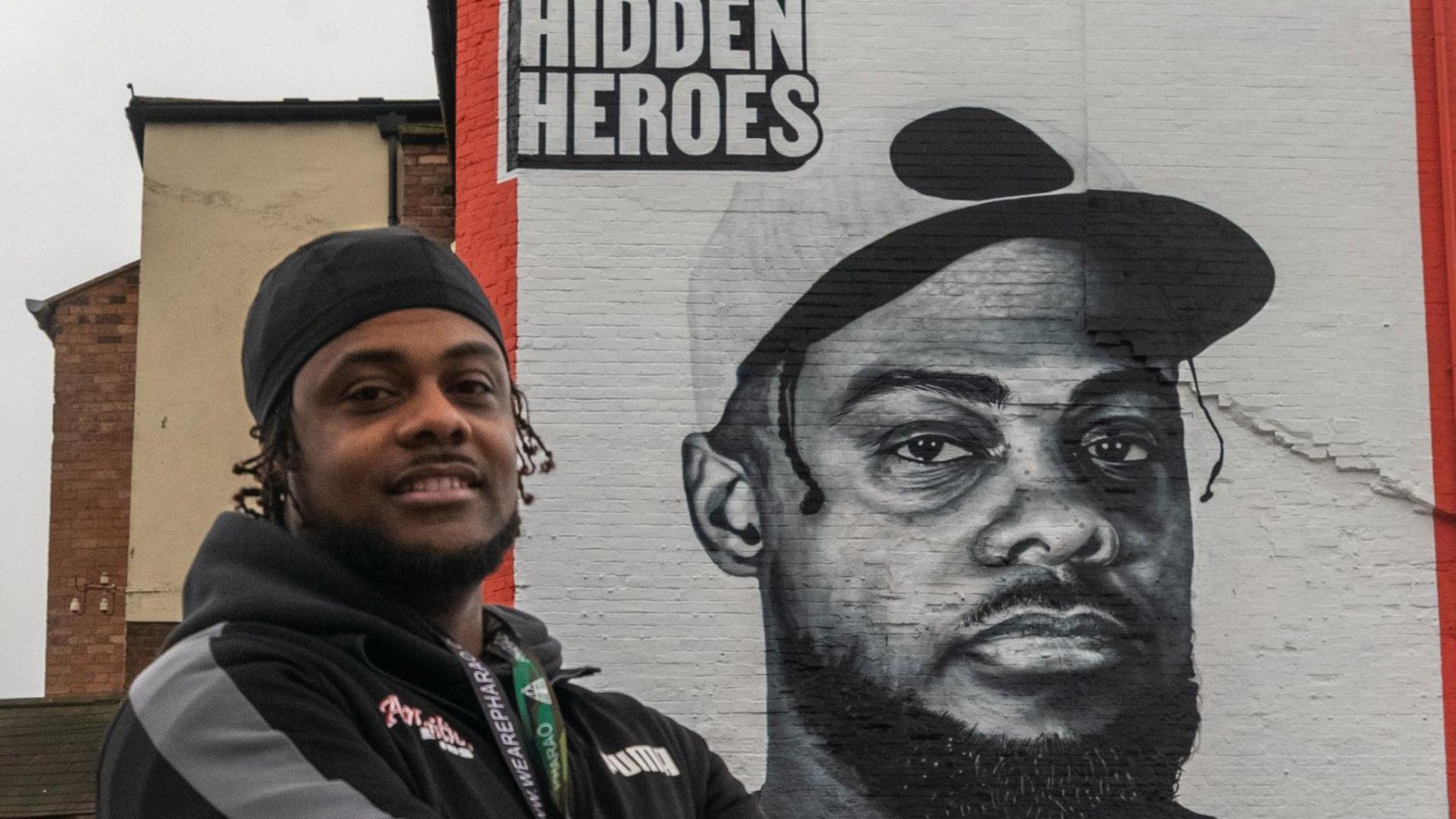 Malachi Nunes posing next to a street art mural celebrating his charity Ambitious Lives