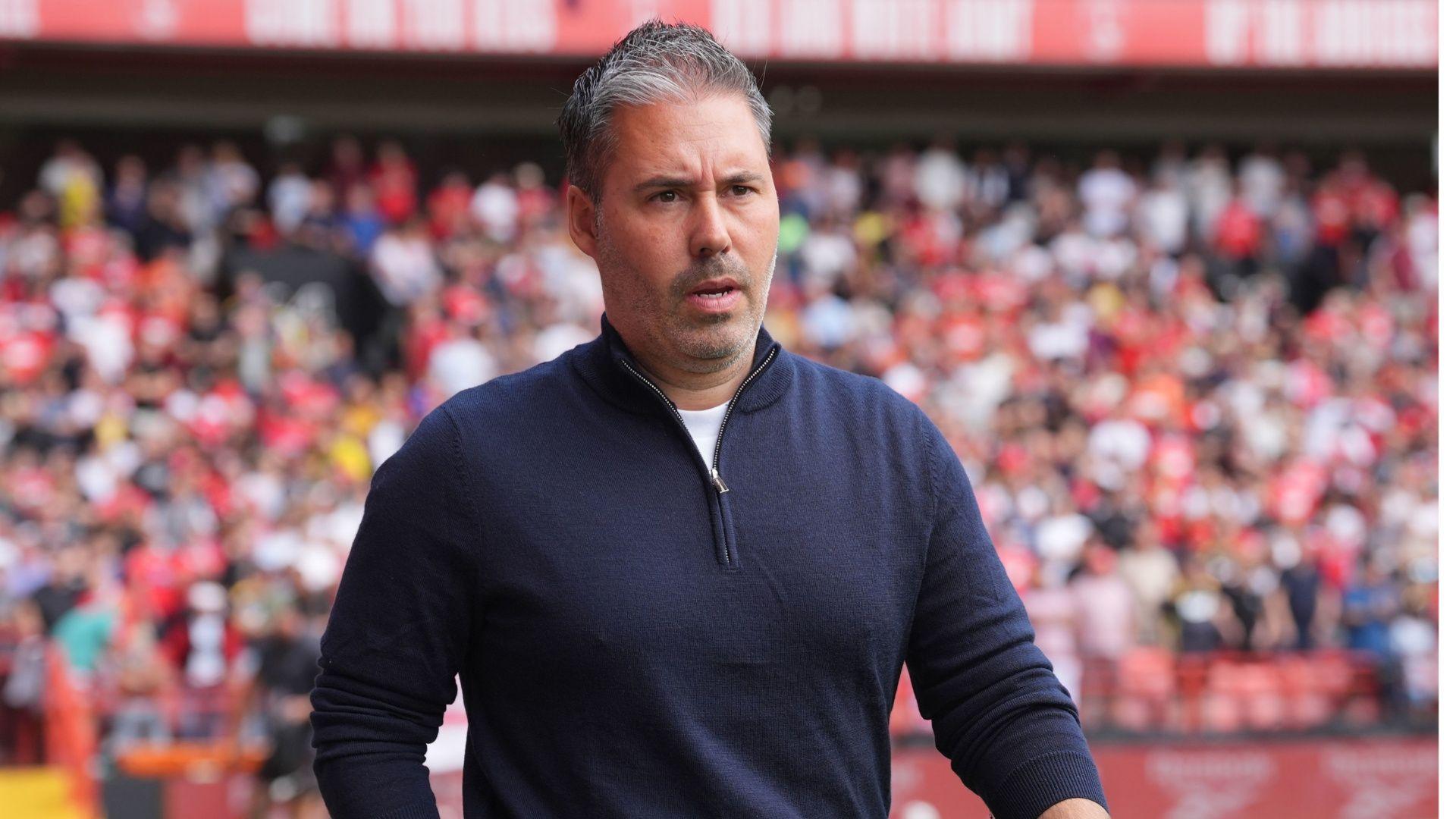 Leicester city manager Marti Cifuentes looks ahead with a determined expression on his face. he stands in front of a stadium crowd and wears a navy quarter zip top.