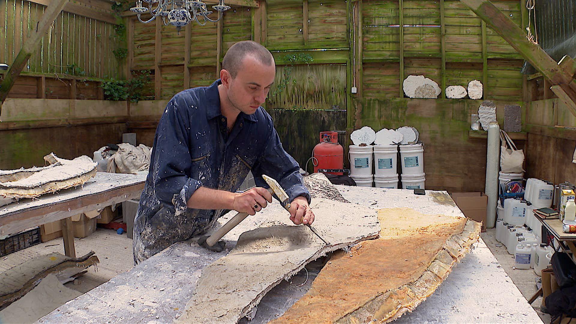 Artist, Robin Sullivan, using a hammer and chisel to take off the edges of one of the bronze panels which will cover the monoliths