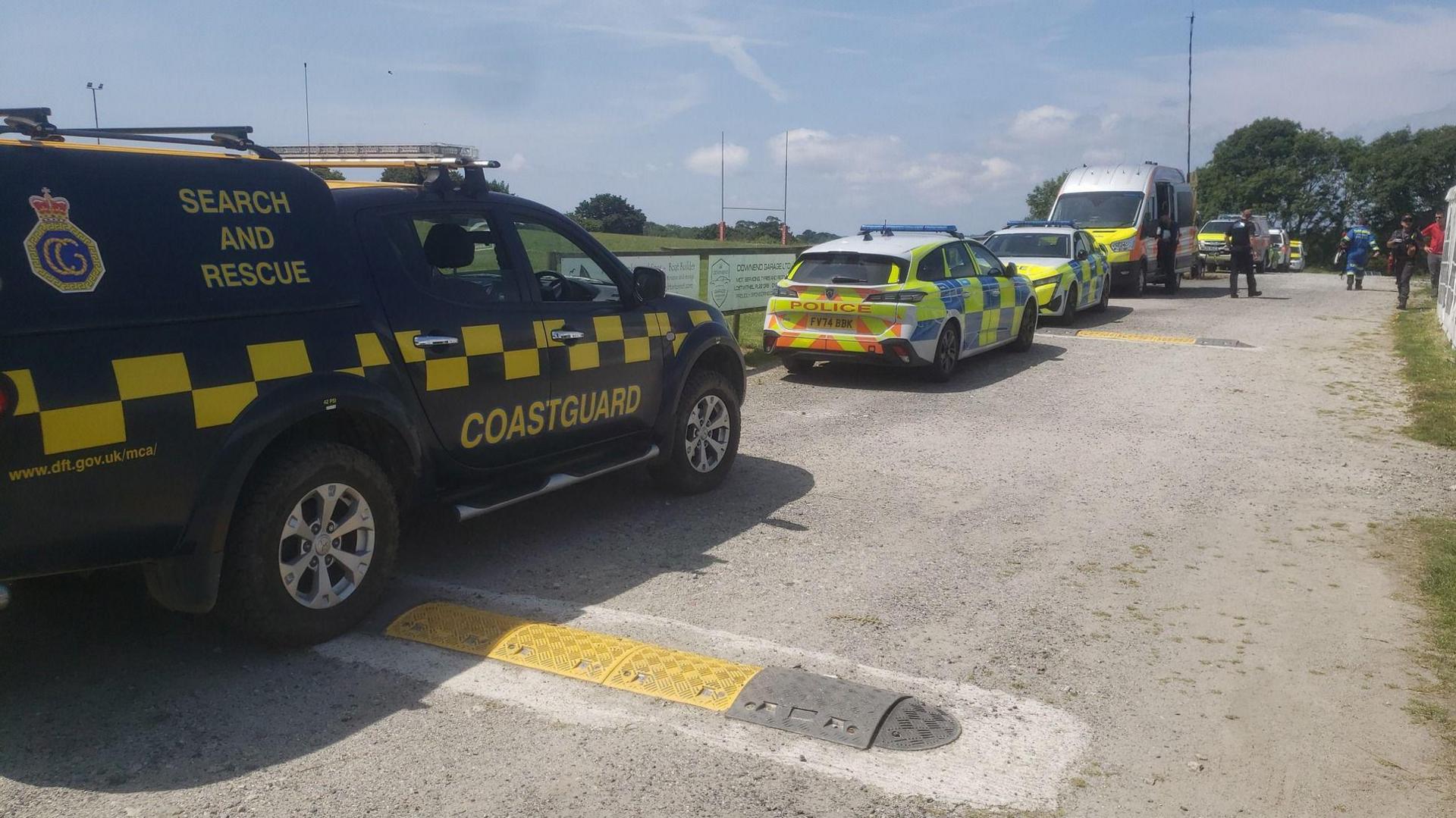 A dark blue HM Coastguard vehicle is parked up next to multiple police cars next to a rugby pitch.