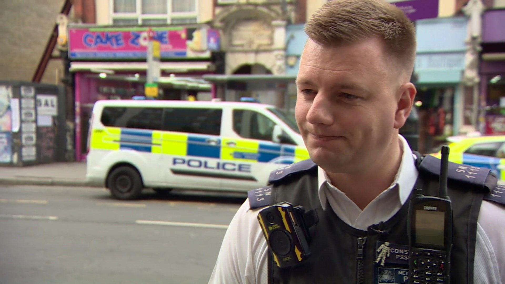 PC Joe West stands in uniform across the street from a Met Police van