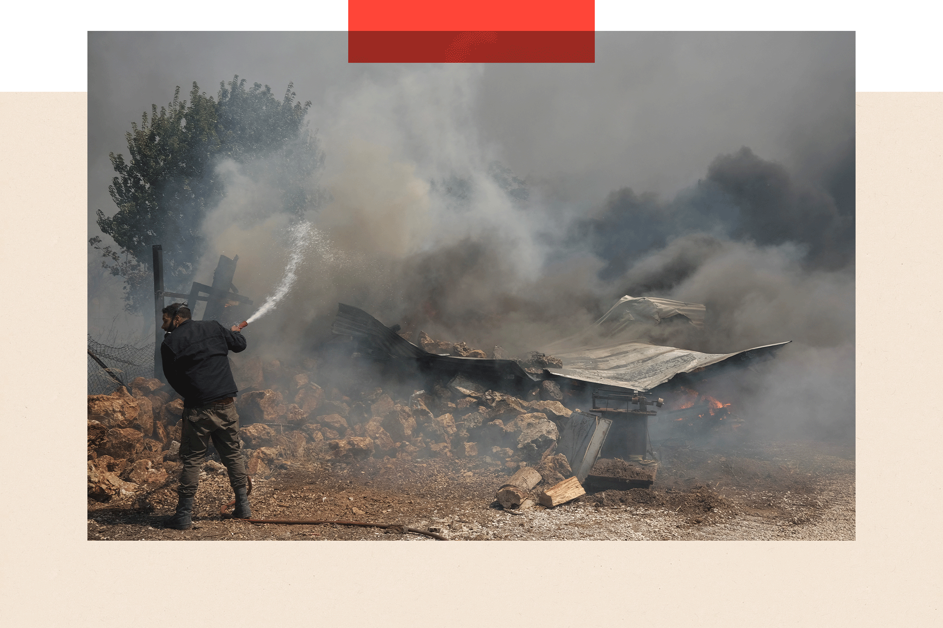 A man tries to extinguish a fire burning a house as a wildfire burns in Nea Penteli, Greece