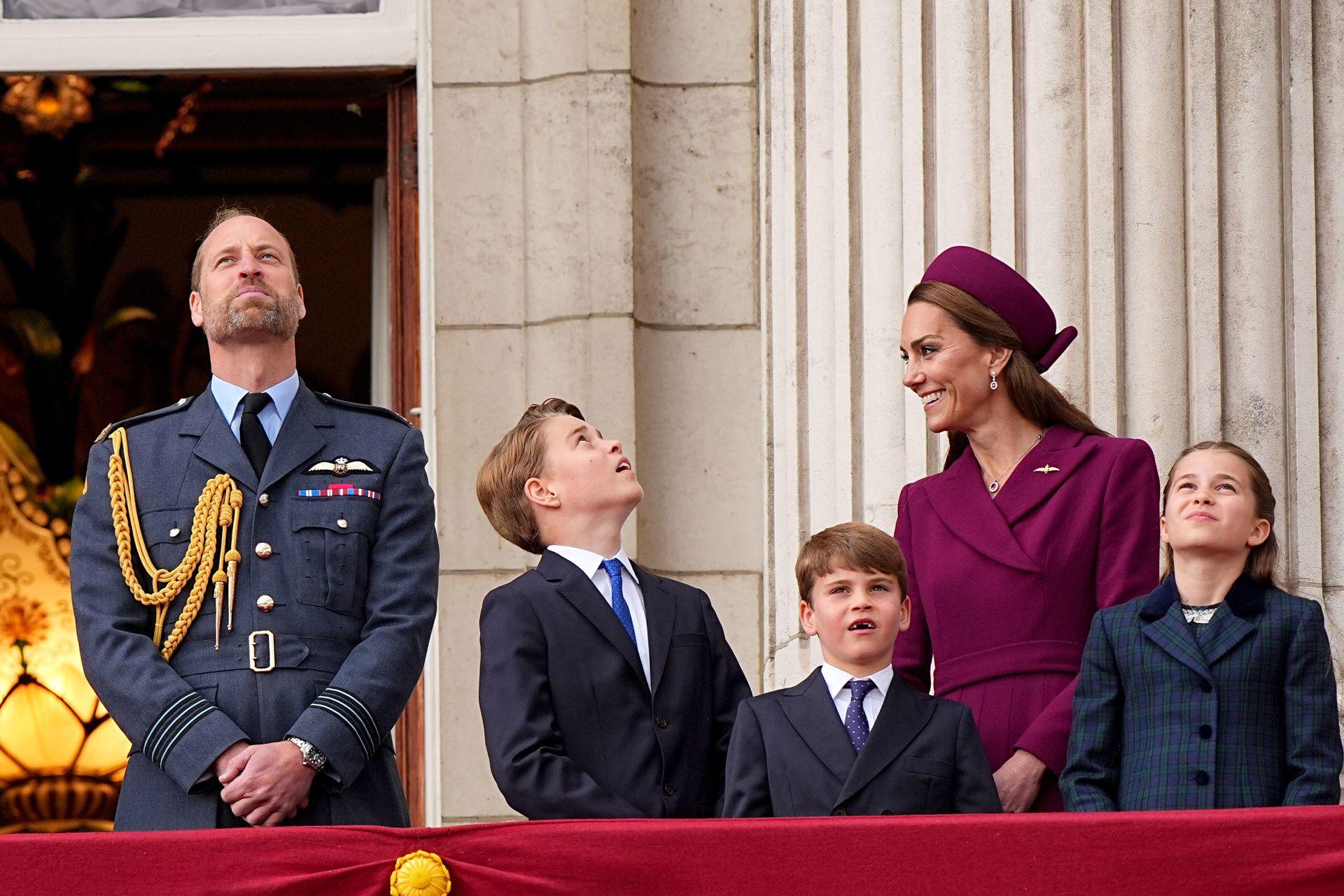 William, Prince of Wales looks up to the sky while Catherine, Princess of Wales laughs and their three children look up to the sky as they stand on the balcony of Buckingham Palace.