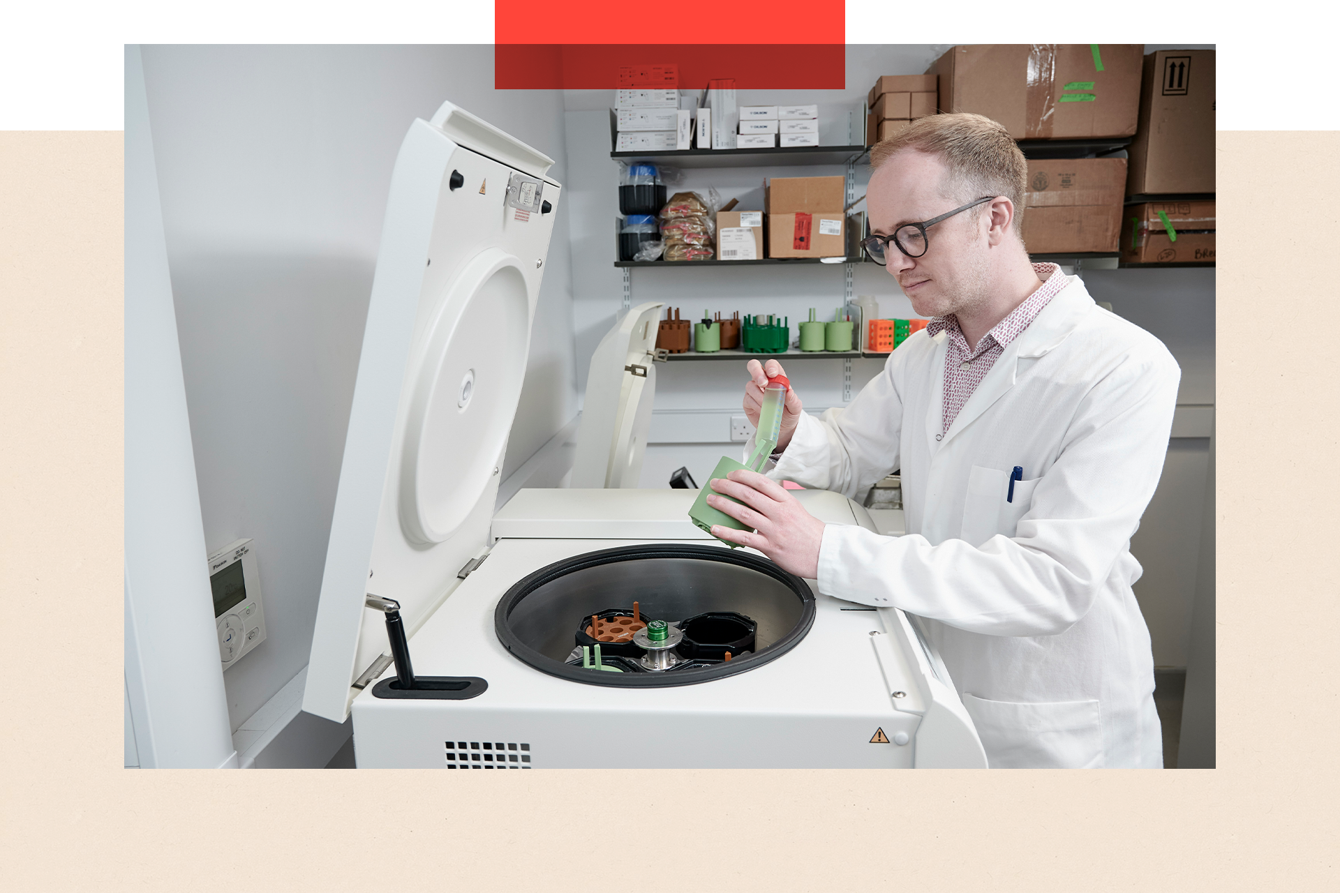 A white machine with a circular hatch contains scientific equipment. A man in a white coat is leaning over the hatch and working with some of the equipement