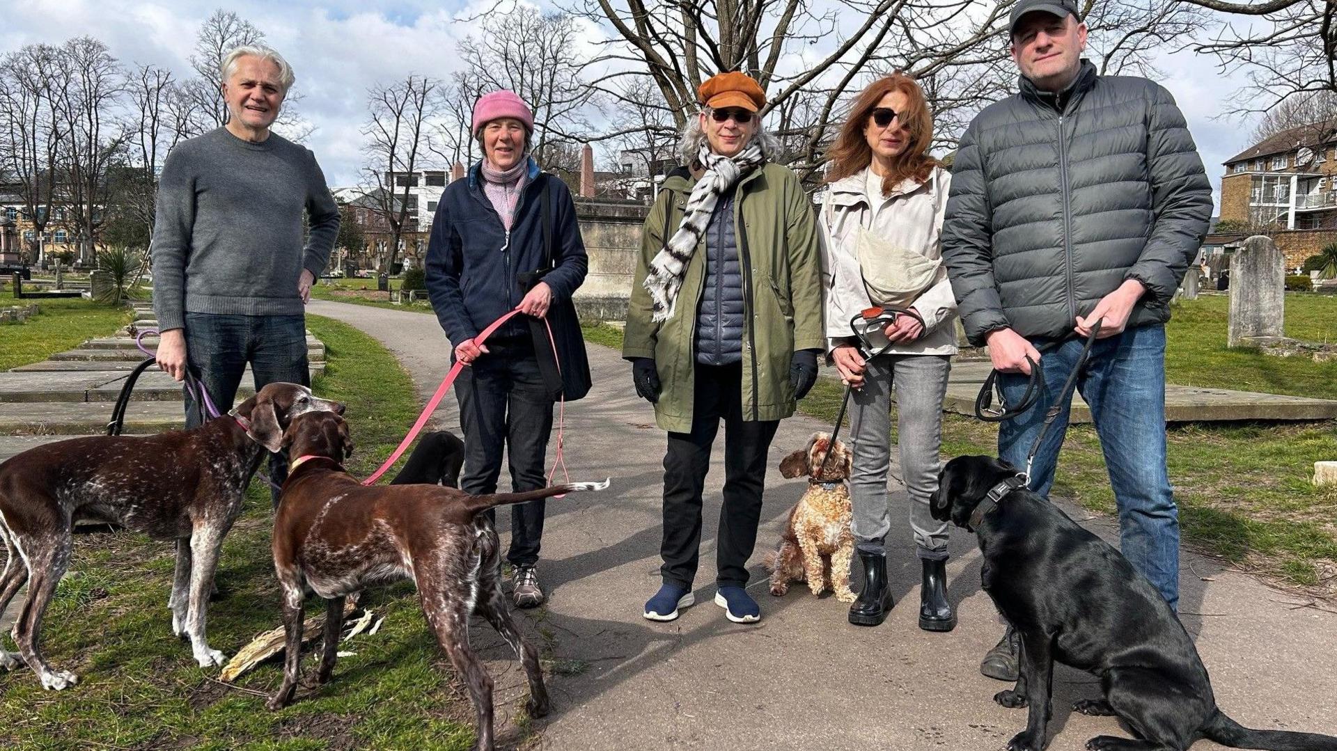 A group of five people with dogs on leads in the cemetery