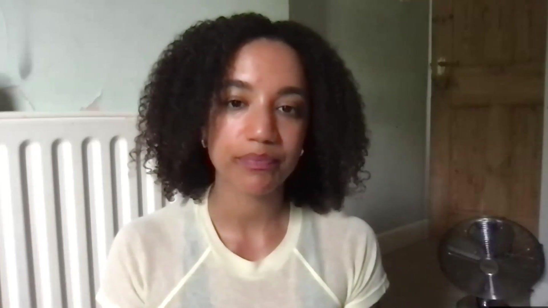 Close up of woman's face who is sitting in lounge near radiator. She has black curly hair and brown eyes.