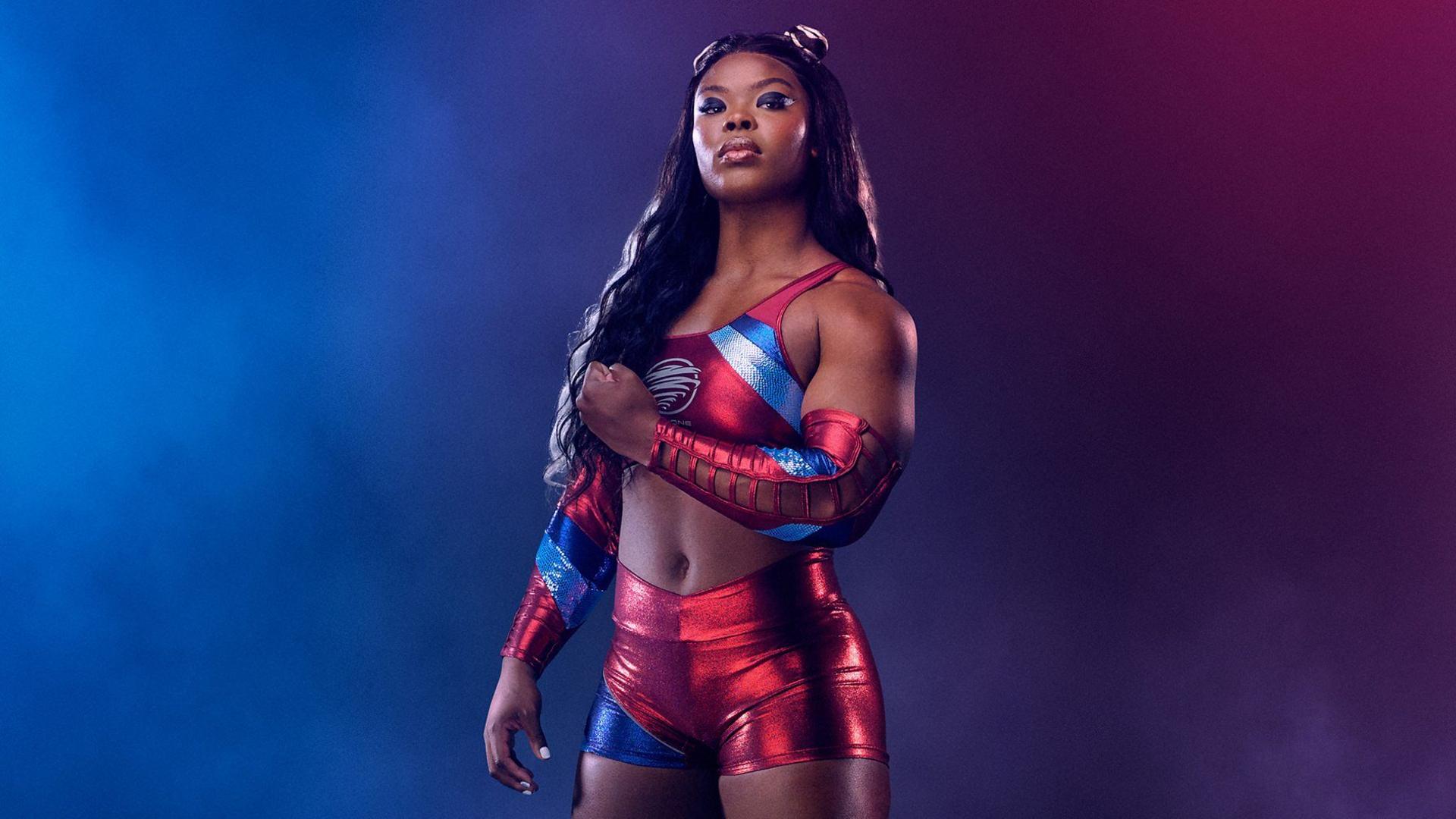 An athlete tenses her muscles as she stares into the camera, wearing a bright red and blue shiny outfit.