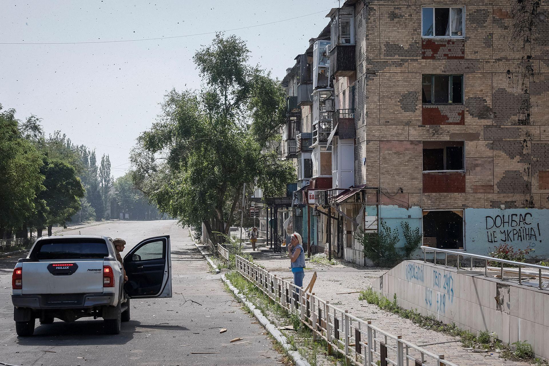 A resident stands on a street outside an apartment block, communicating with a police officer who is poking their head out of a police van, in Toretsk near the frontline in Donetsk region in July 2024. 