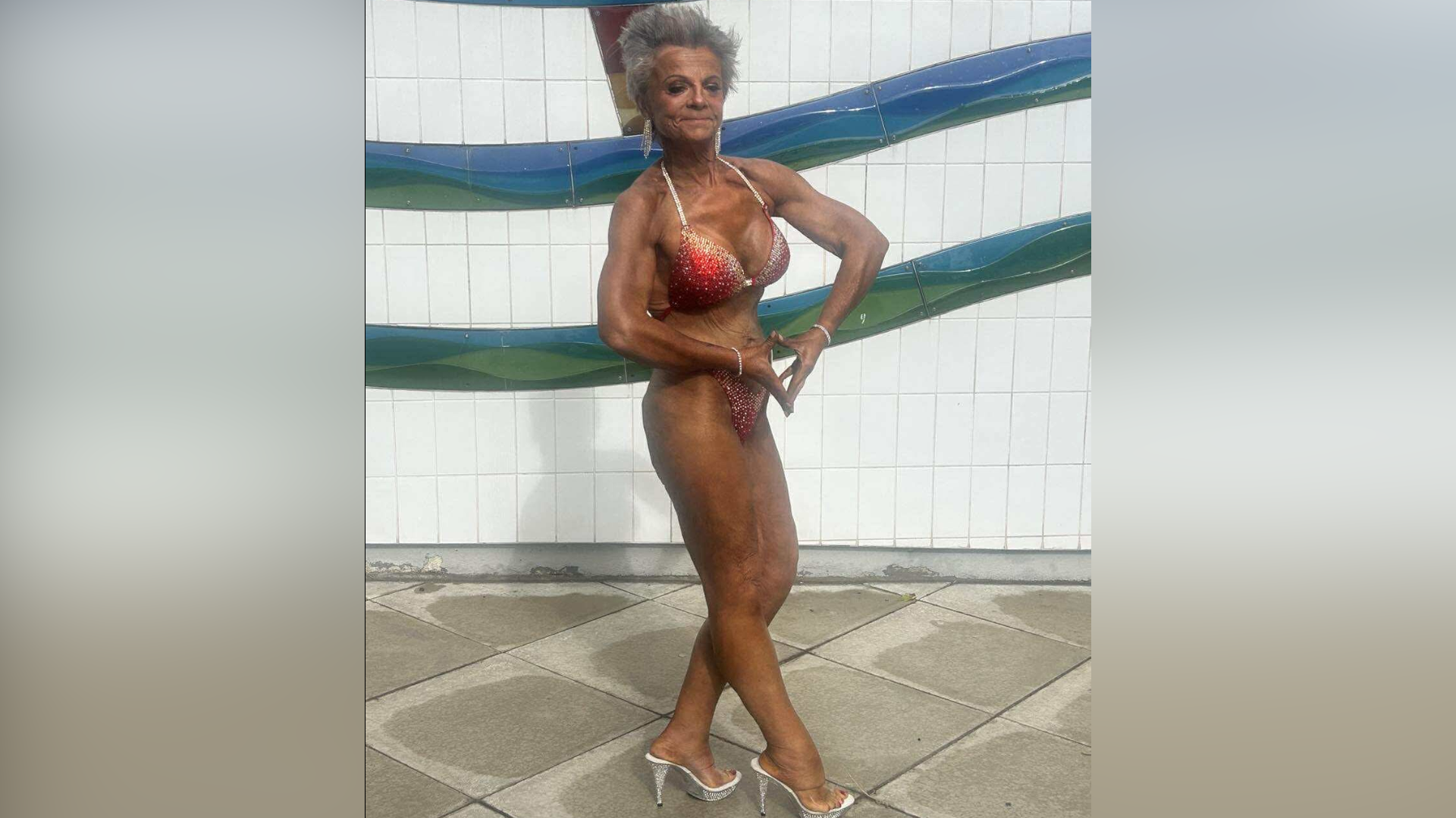 Ms Smith is pictured prior to a bodybuilding competition. She wears a red bikini and silver heels and she has fake tanned her body. She poses and flexes her arms to show off the muscle definition.
