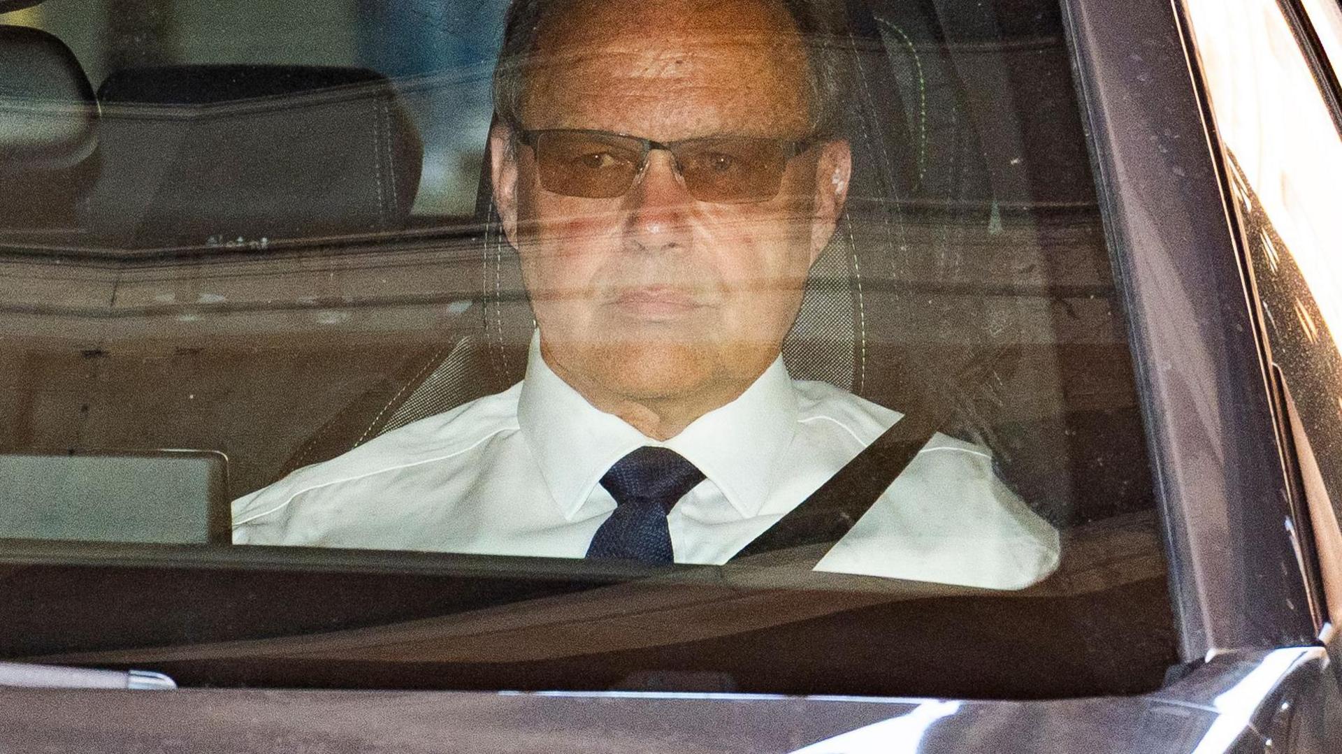 Razzell leaving court sat in a car and wearing dark glasses. He is looking straight ahead and not smiling.