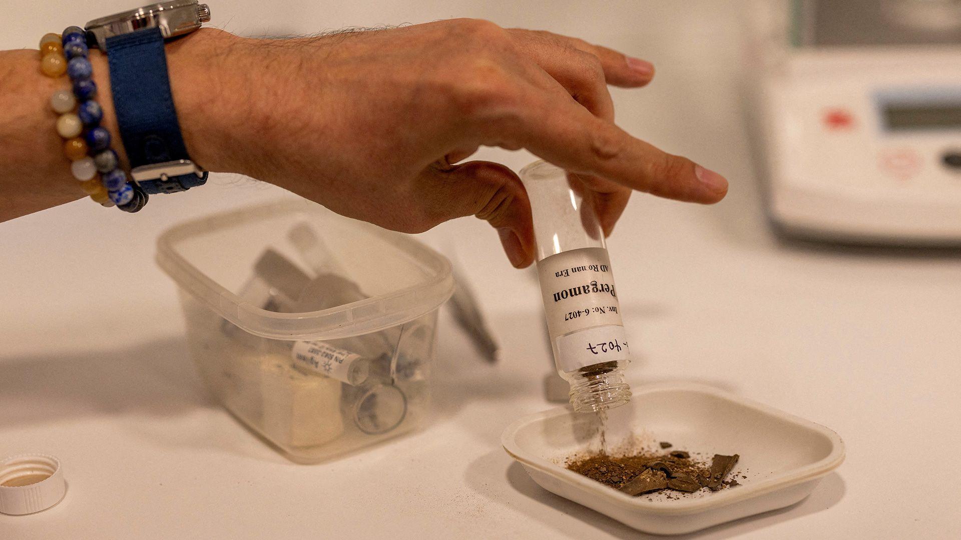 A person emptying a vial with dusty brown remains inside