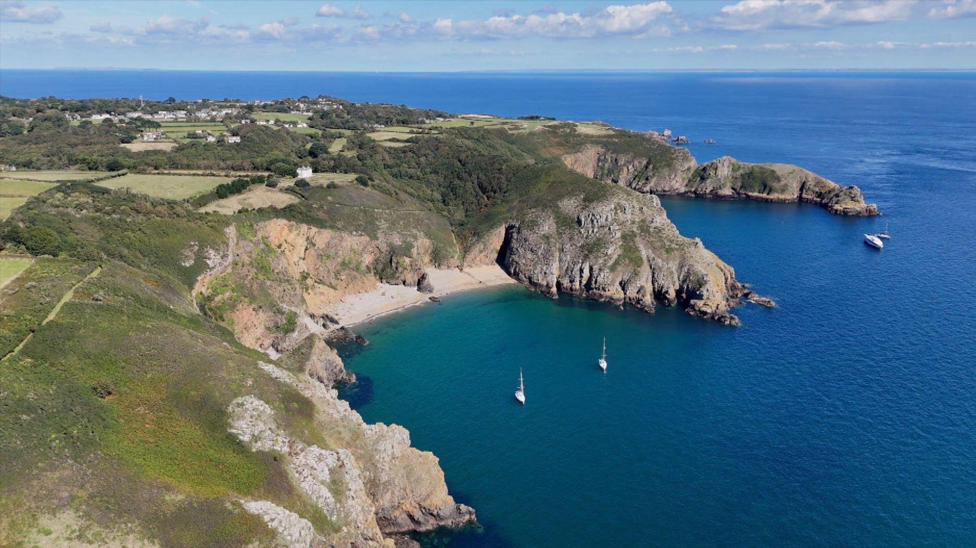 A birds-eye view of Sark. To the left is the land and on the right is the sea with a few boats.