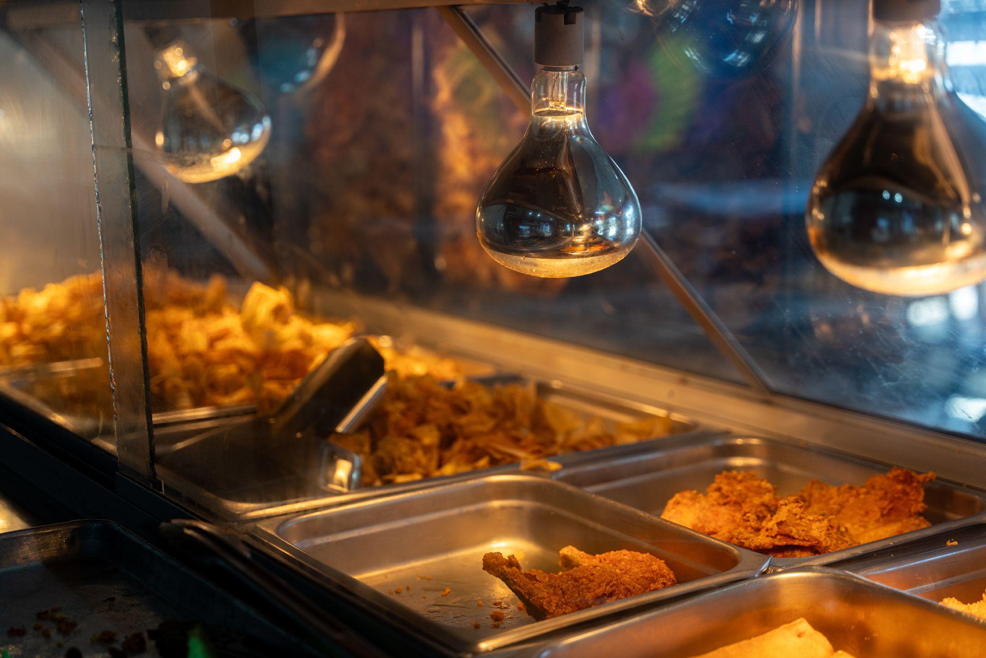 Deep-fried pork, chicken and plantain is displayed in trays underneath a heat lamp in Comayagua