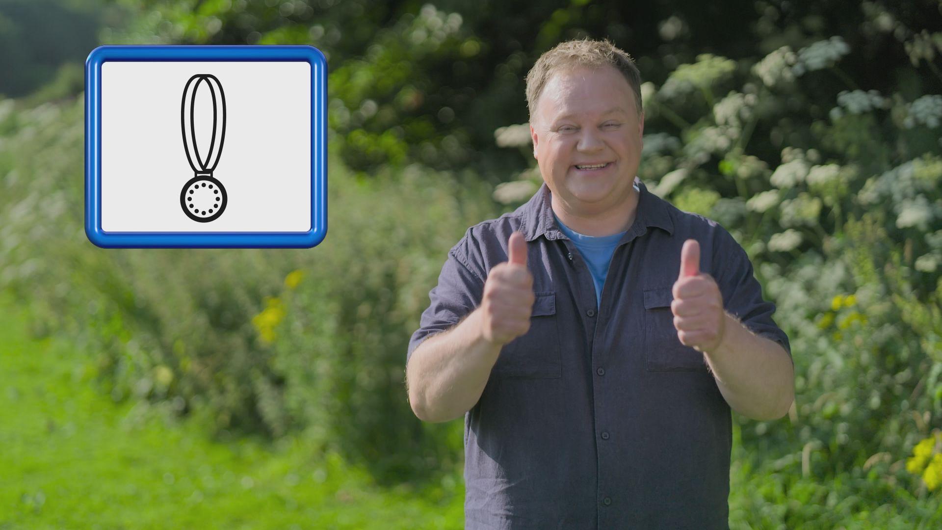 Justin Fletcher pictured with the Makaton symbol for "medal" 