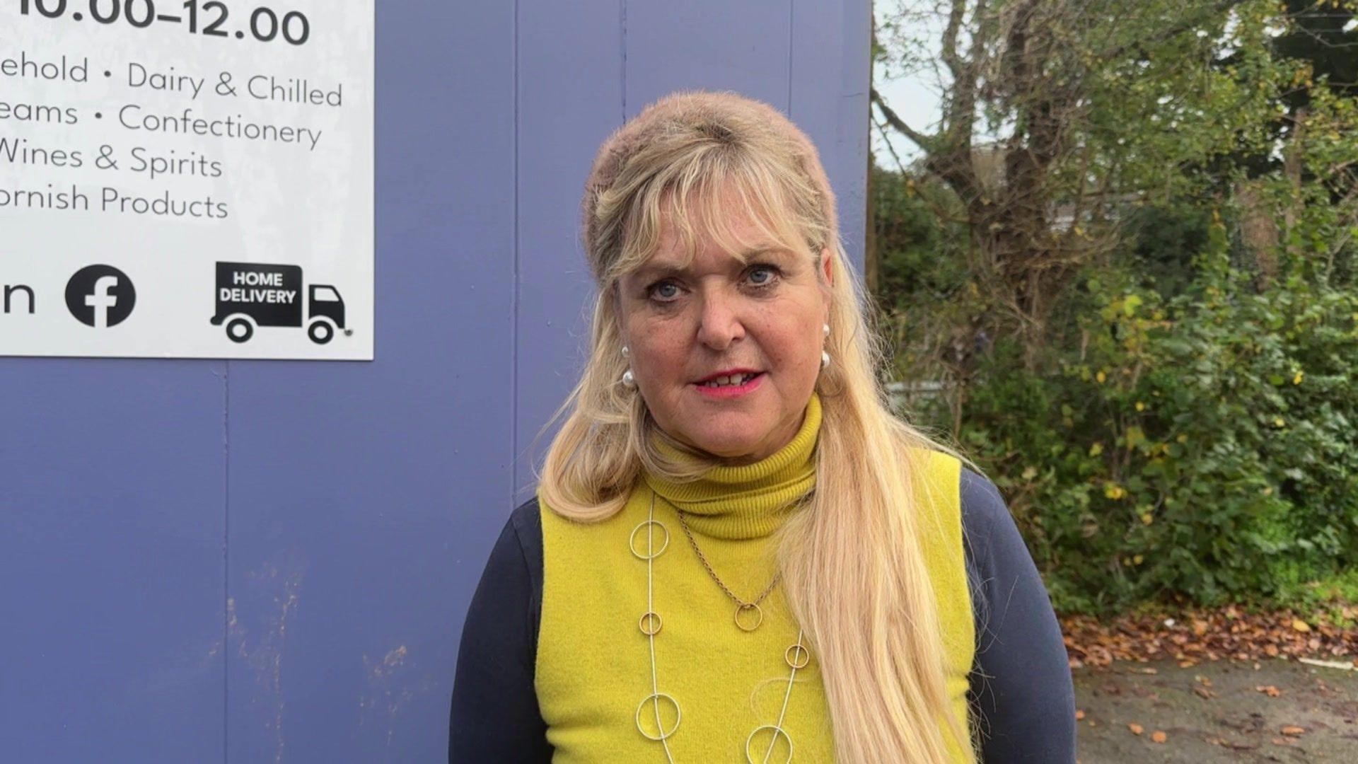 A woman with long blonde hair wearing a yellow top with black sleeves. 