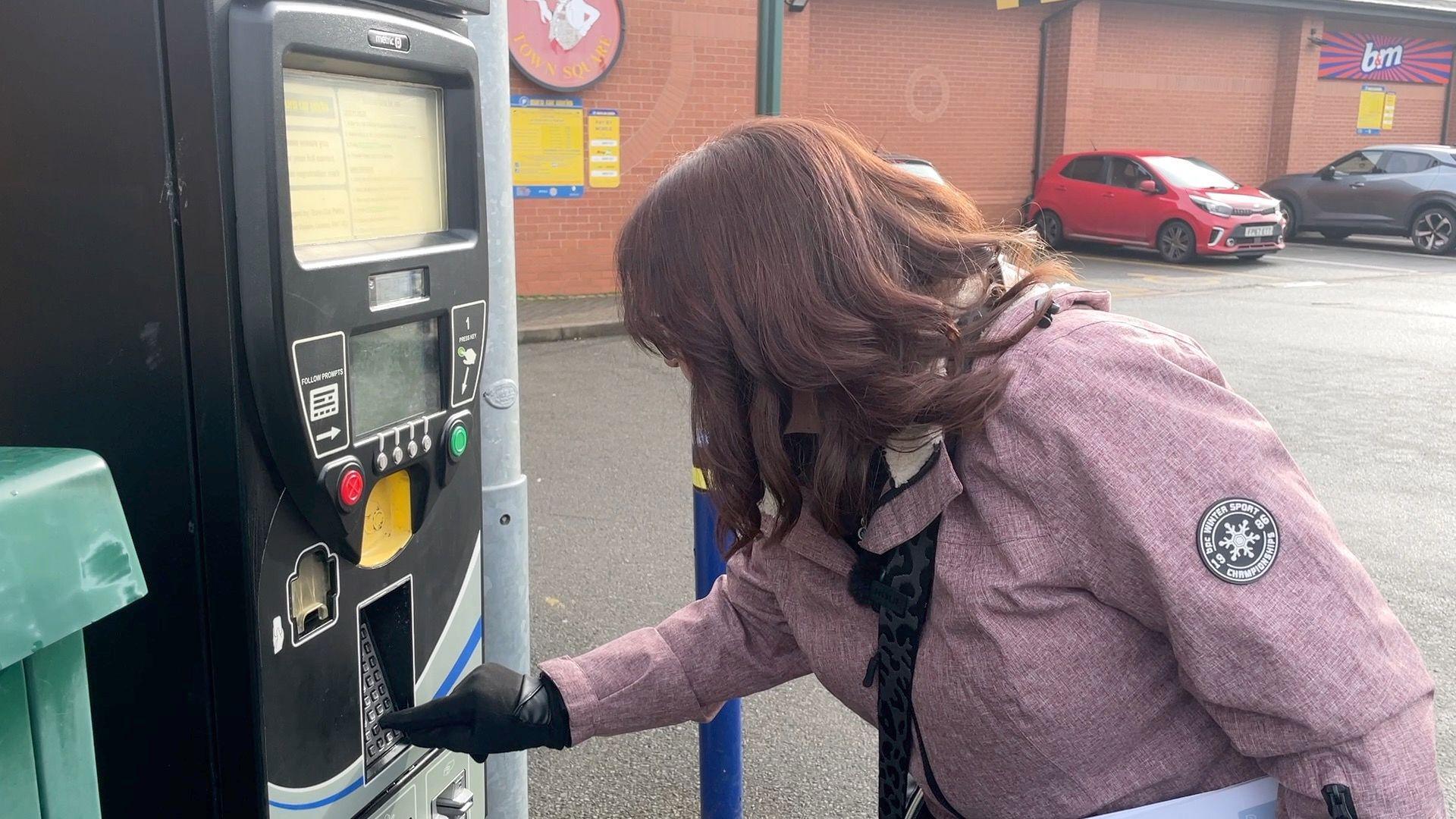 A woman uses a payment machine at Syston Town Square car park