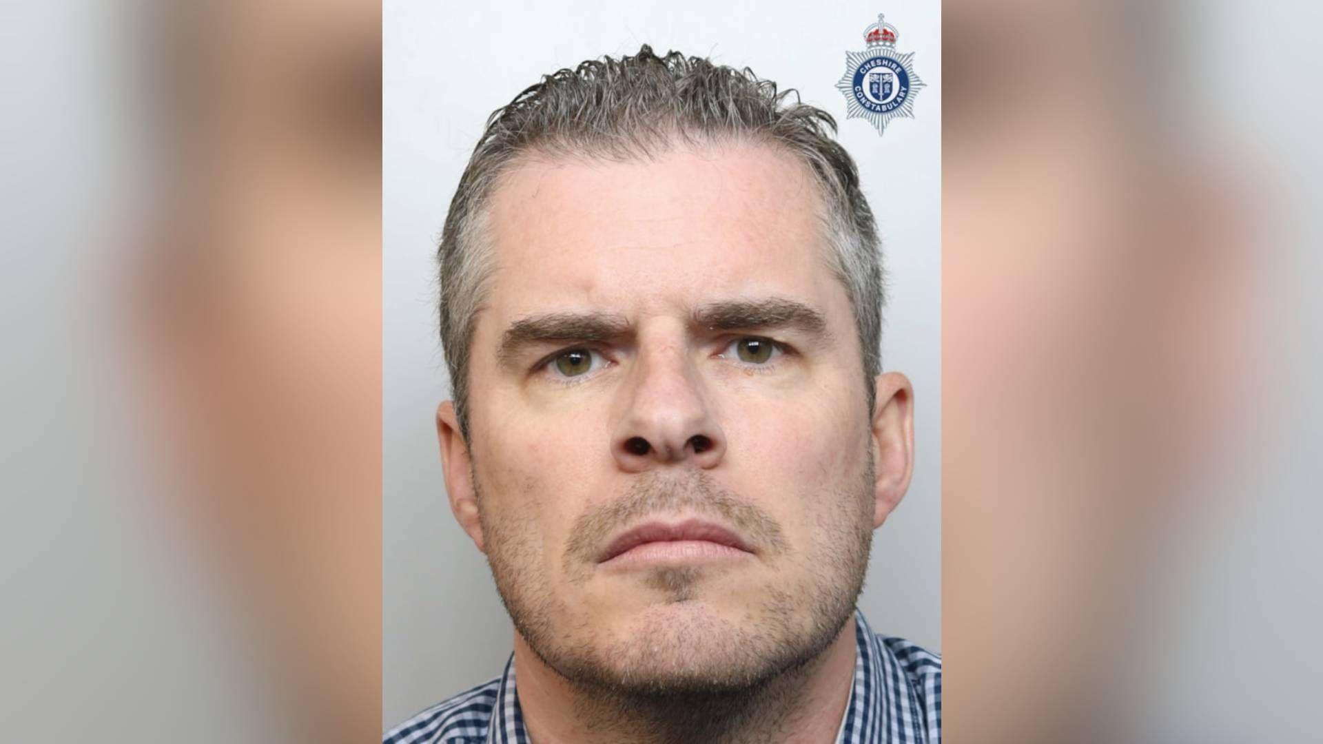 Mugshot of Simon Clark, 46, who has grey short hair and a grey beard. He frowns at the camera.