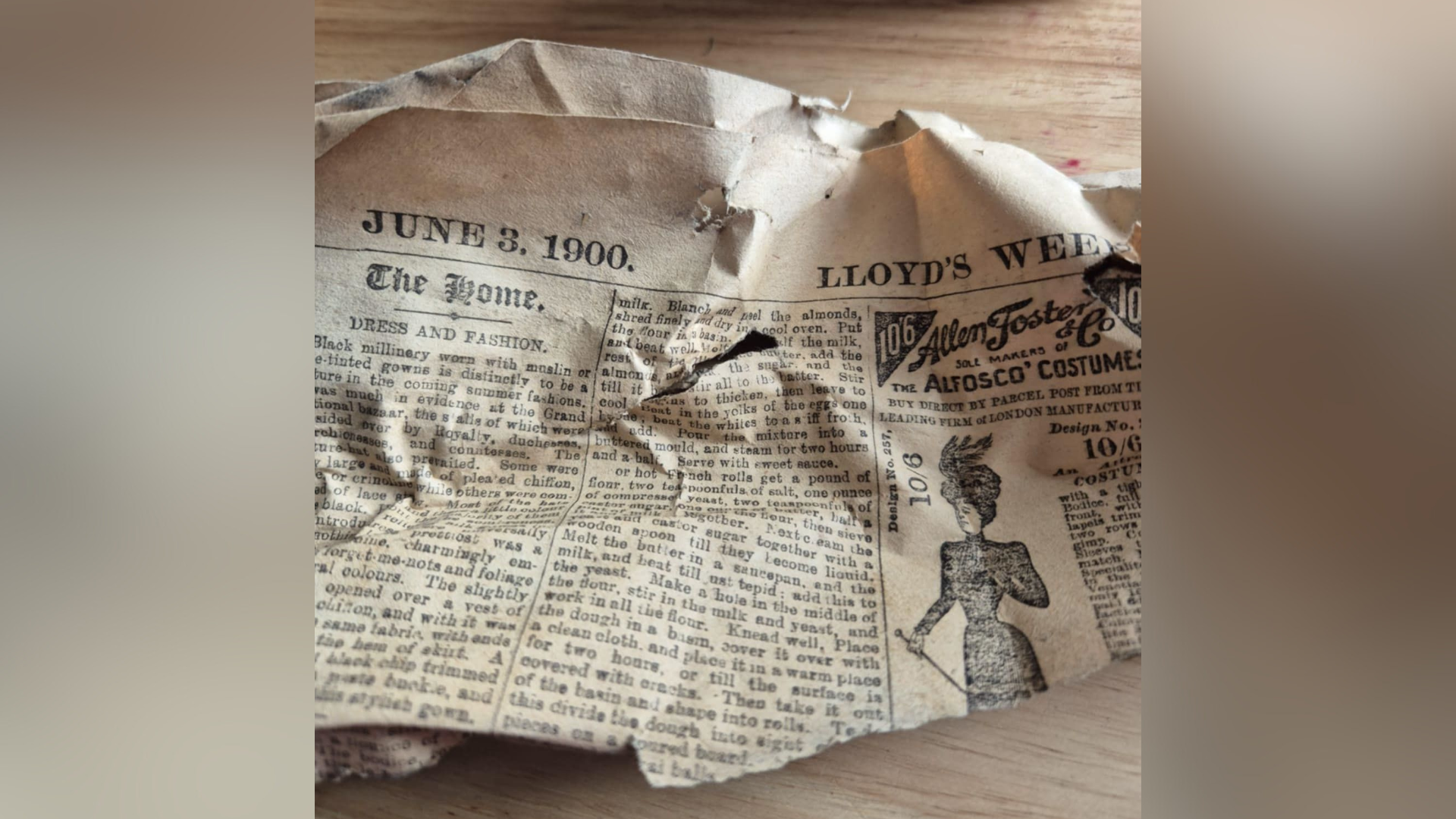 A scrunched up piece of newspaper with columns or words on it. A picture of a woman sits on the right hand side. The header of the newspaper has the date "June 3, 1900".
