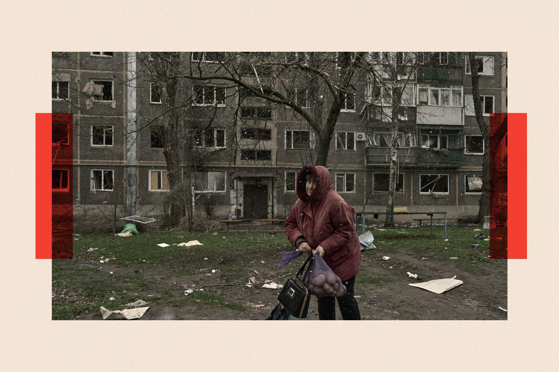 A woman carries a sack of potatoes by damaged residential buildings in Pokrovsk, Ukraine
